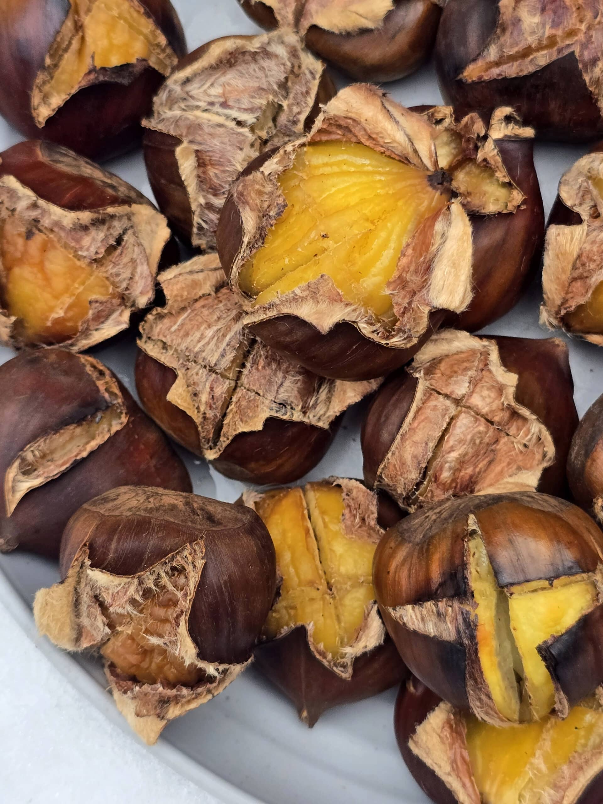 A plate of campfire roasted chestnuts on a snowy picnic table.