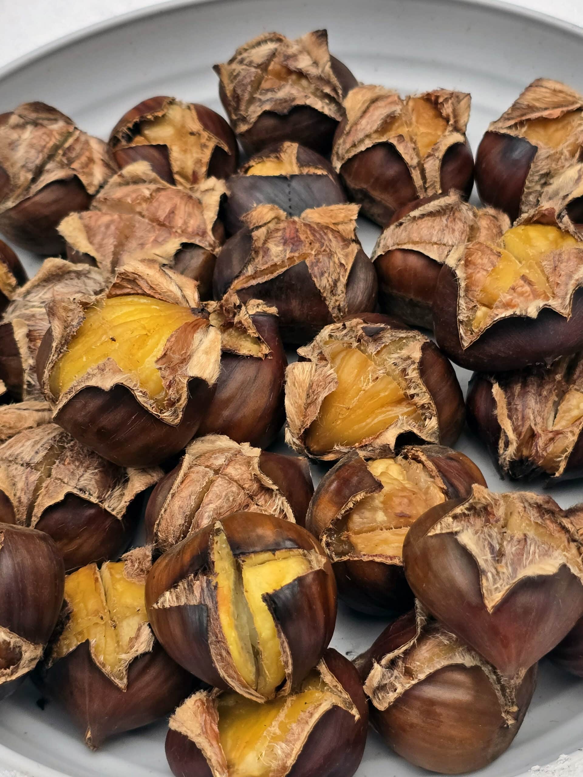 A plate of campfire roasted chestnuts on a snowy picnic table.