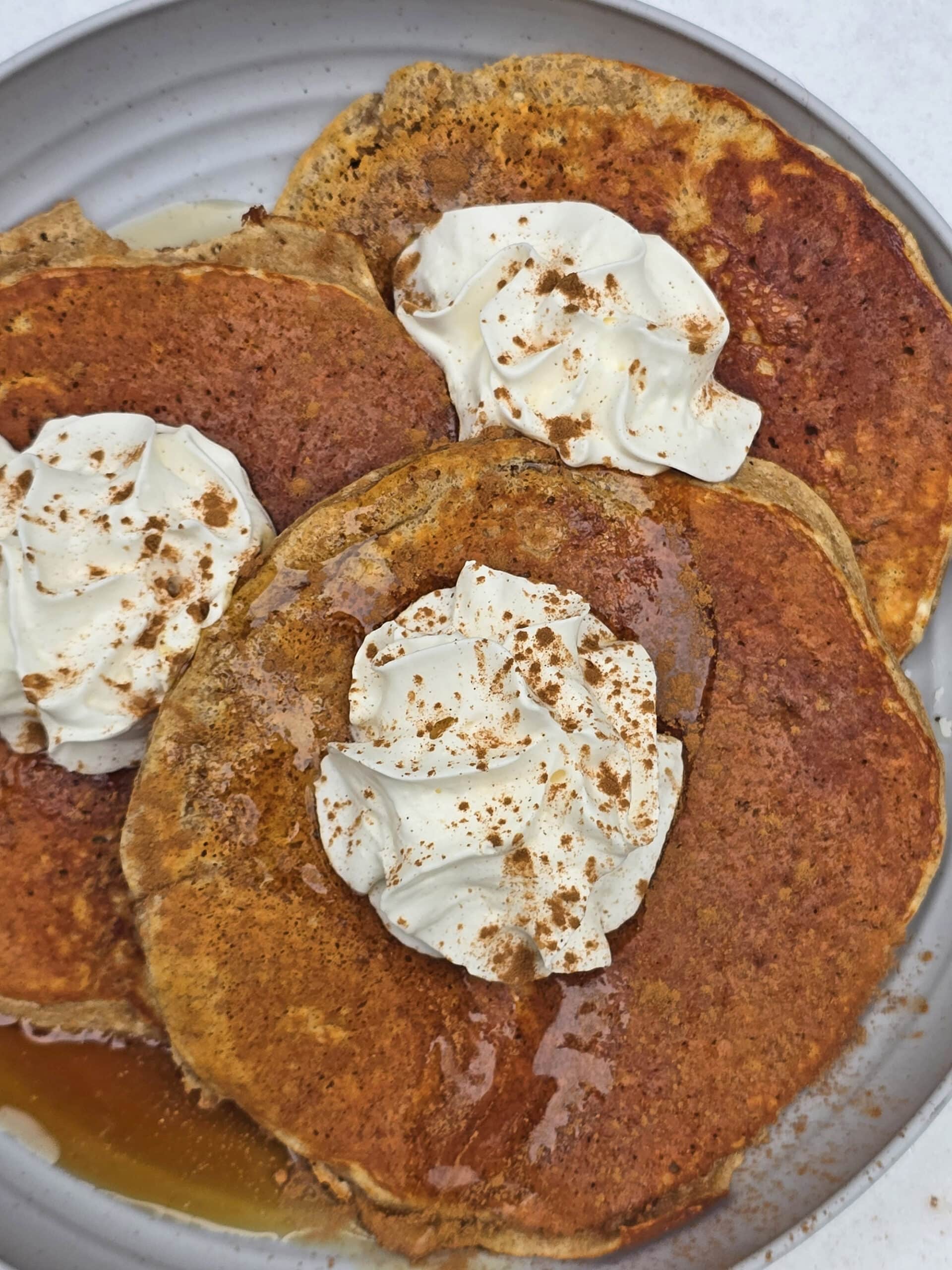 A plate of gingerbread protein pancakes made from homemade gingerbread pancake mix, with maple syrup and whipped cream,  on a snow covered picnic table.