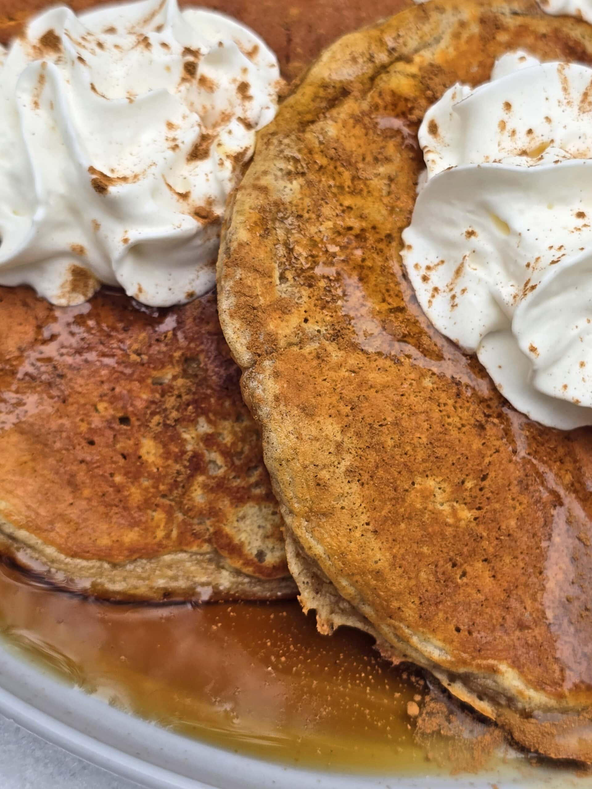 A plate of gingerbread pancakes made from homemade gingerbread pancake mix, with maple syrup and whipped cream,  on a snow covered picnic table.