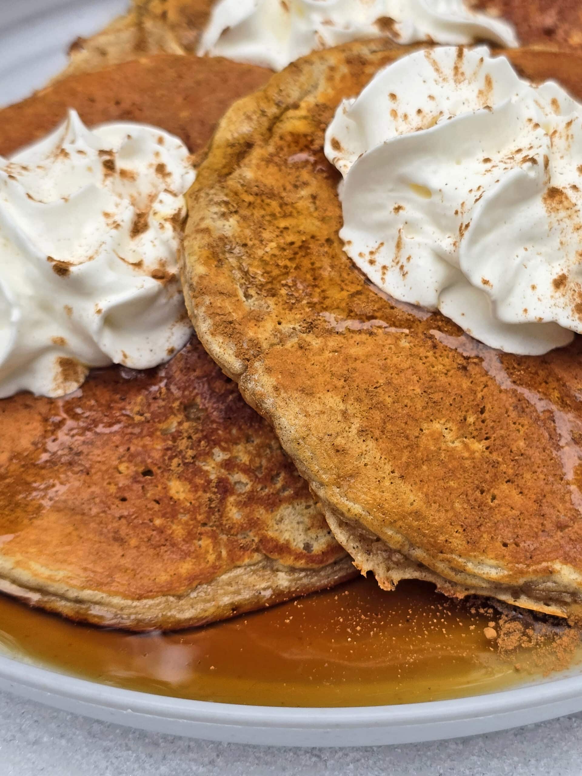 A plate of gingerbread pancakes made from homemade gingerbread pancake mix, with maple syrup and whipped cream,  on a snow covered picnic table.