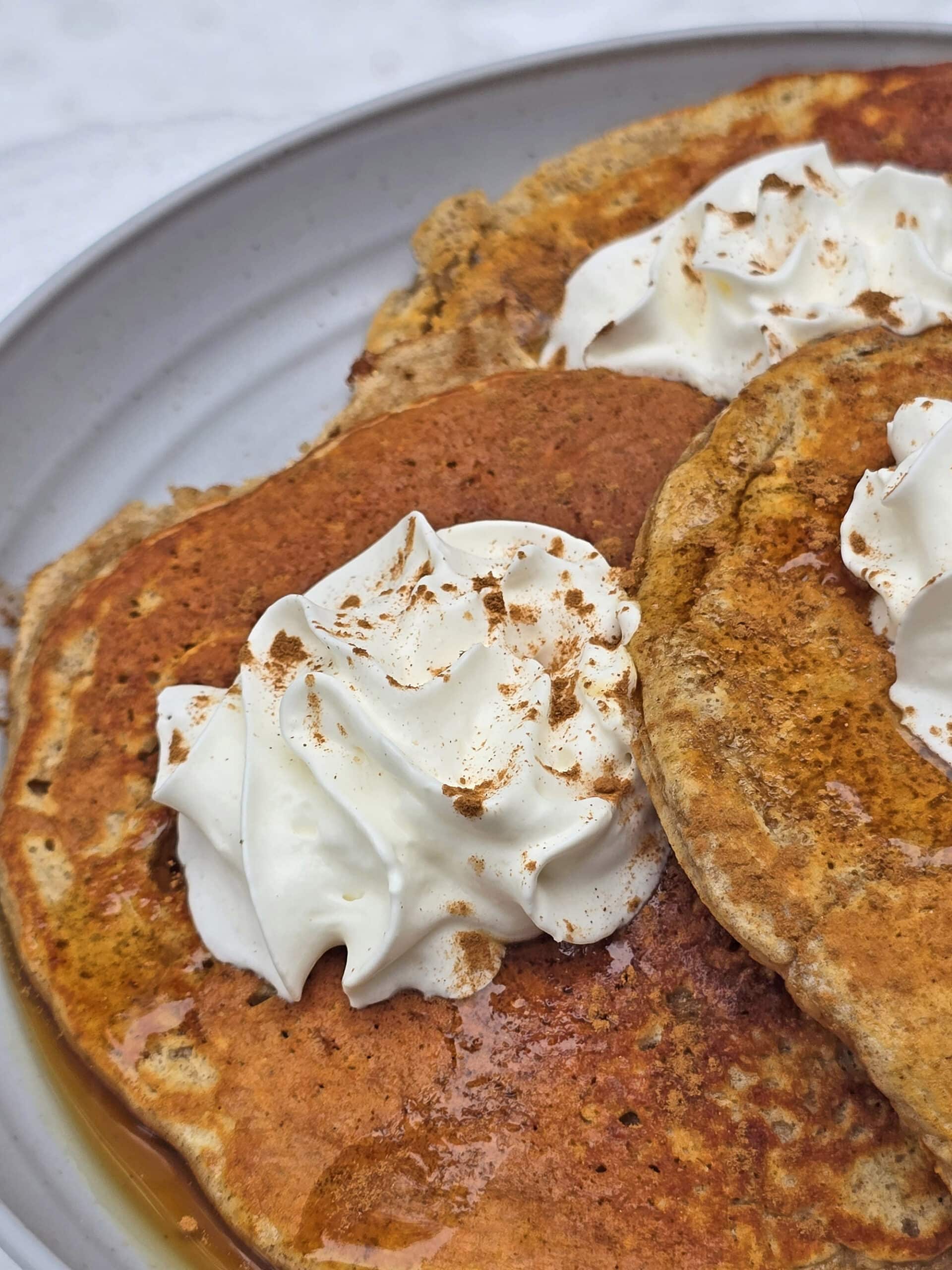 A plate of gingerbread protein pancakes made from homemade gingerbread pancake mix, with maple syrup and whipped cream,  on a snow covered picnic table.