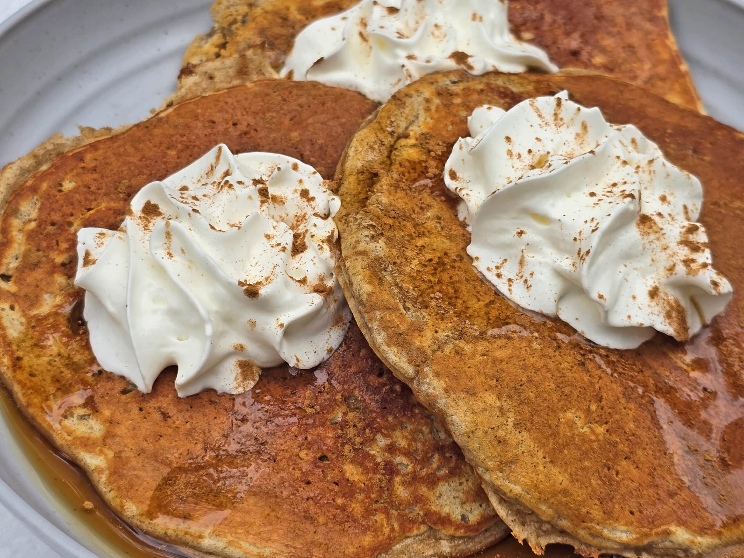 A plate of gingerbread pancakes made from homemade gingerbread pancake mix, with maple syrup and whipped cream,  on a snow covered picnic table.