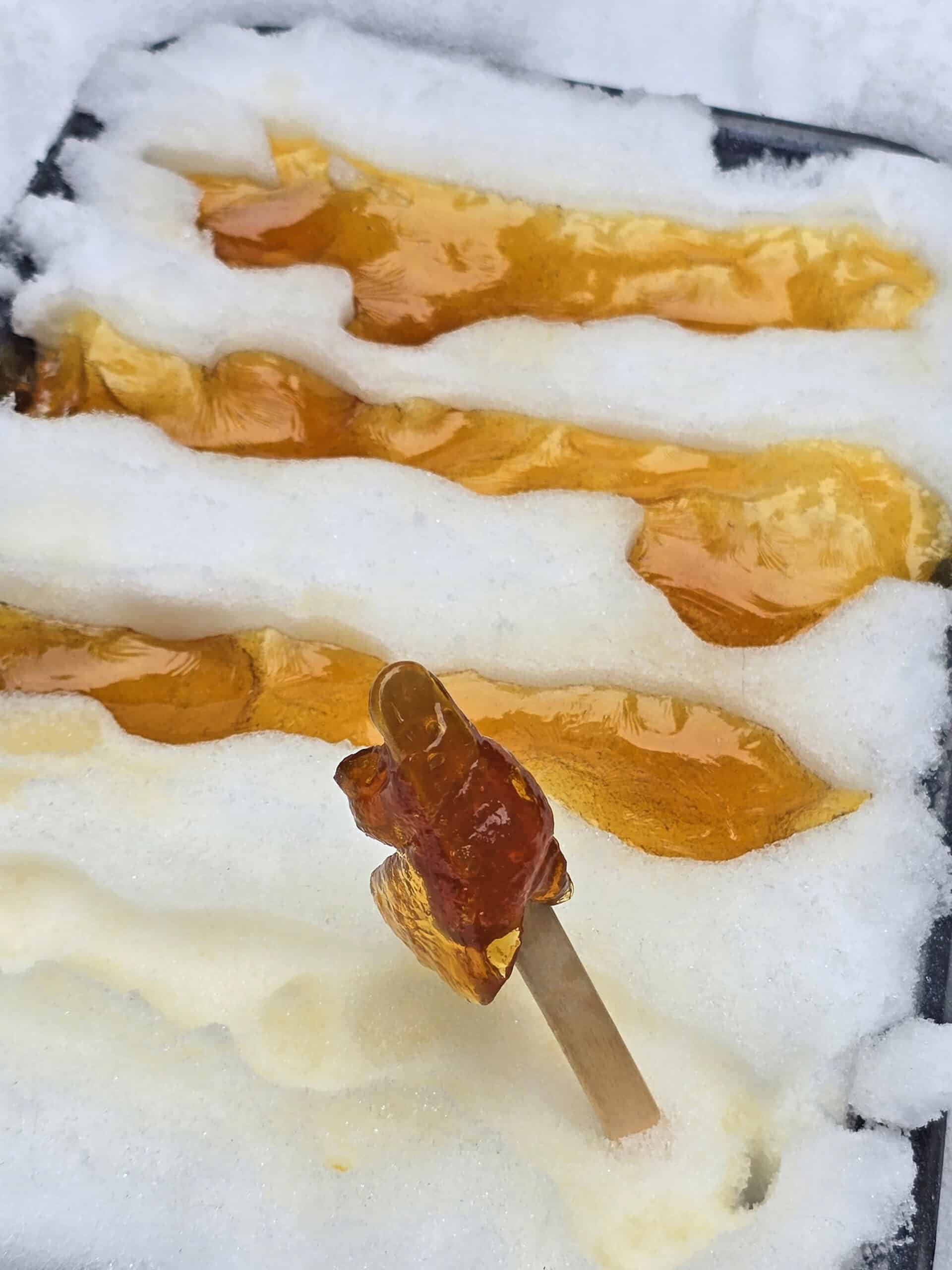 A stick of maple syrup snow taffy in a pan of snow, with lines of maple taffy in it.