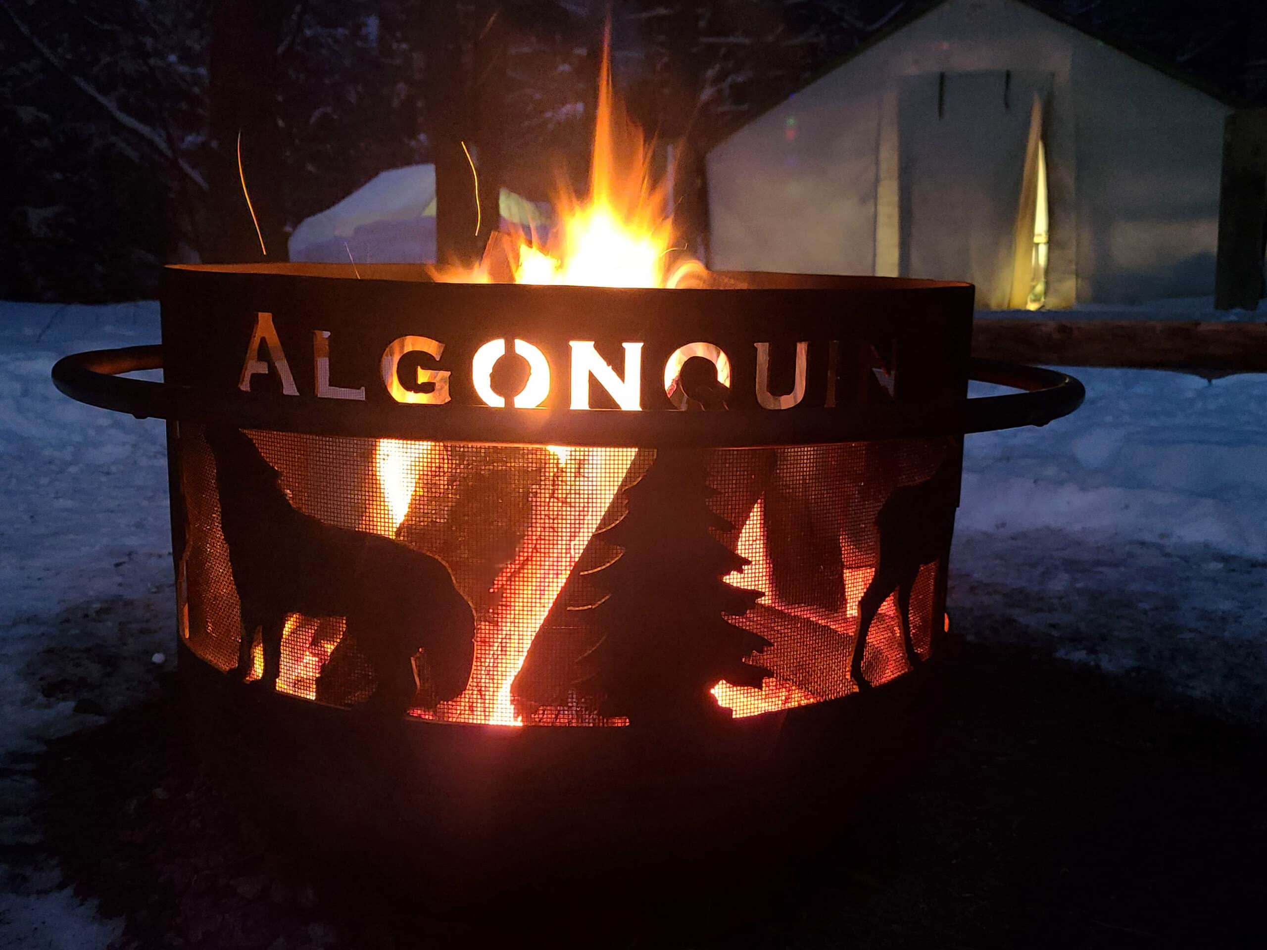 An algonquin provincial park branded fire pit with a campfire at night, in the winter.