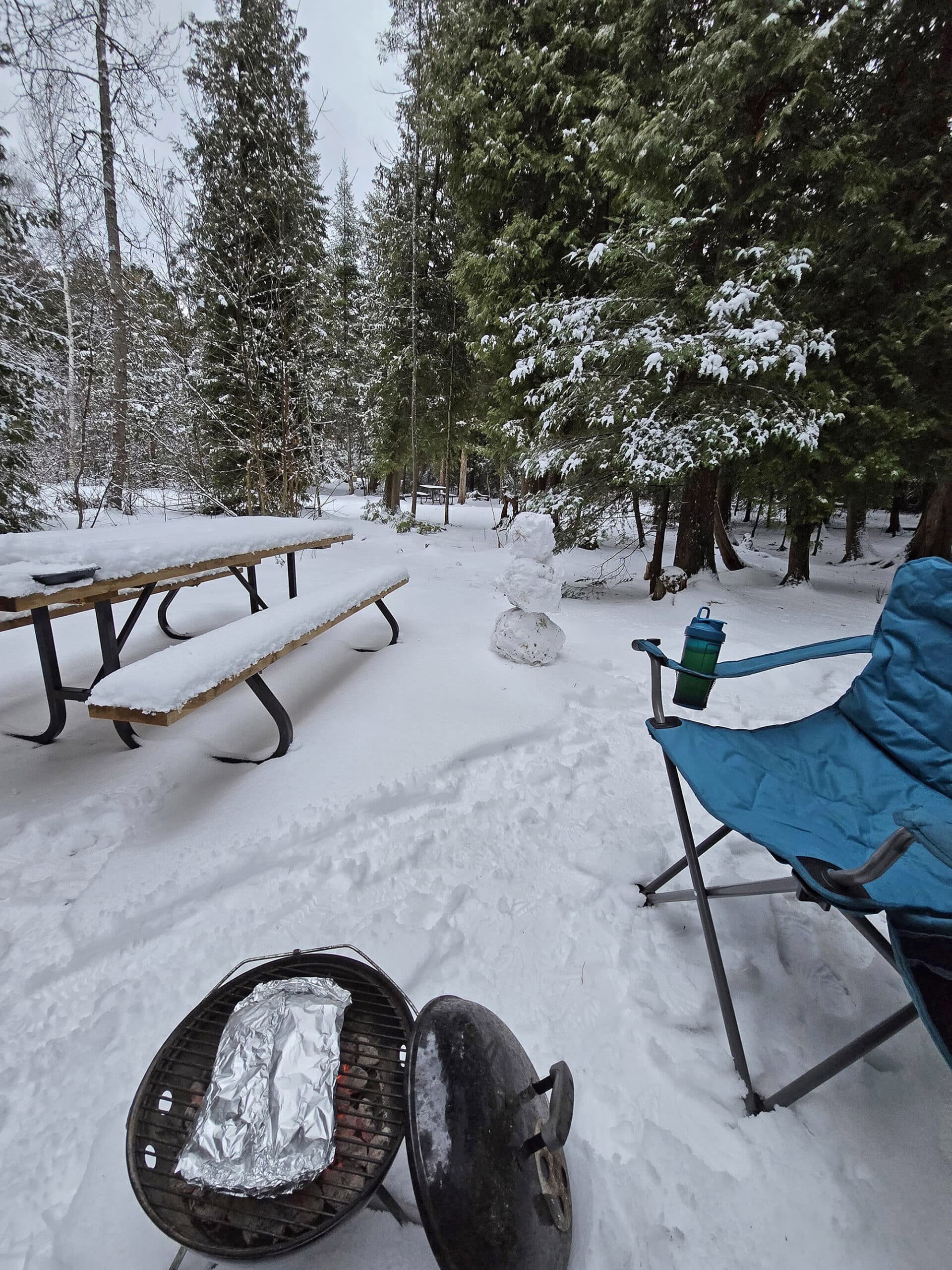 A winter campsite with picnic table, folding chair, and fire pit