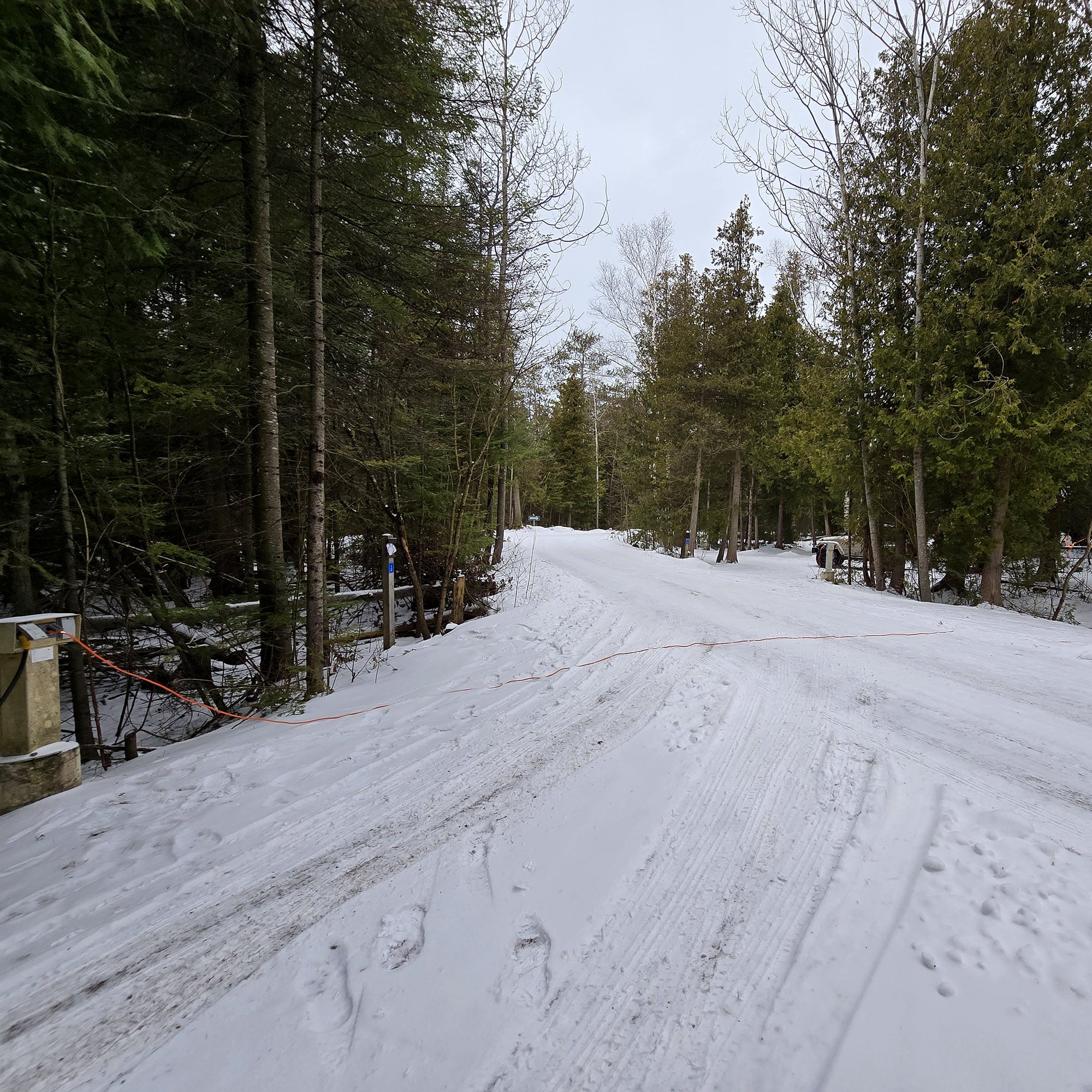 A snow covered campground road with an extension cord draped over it.