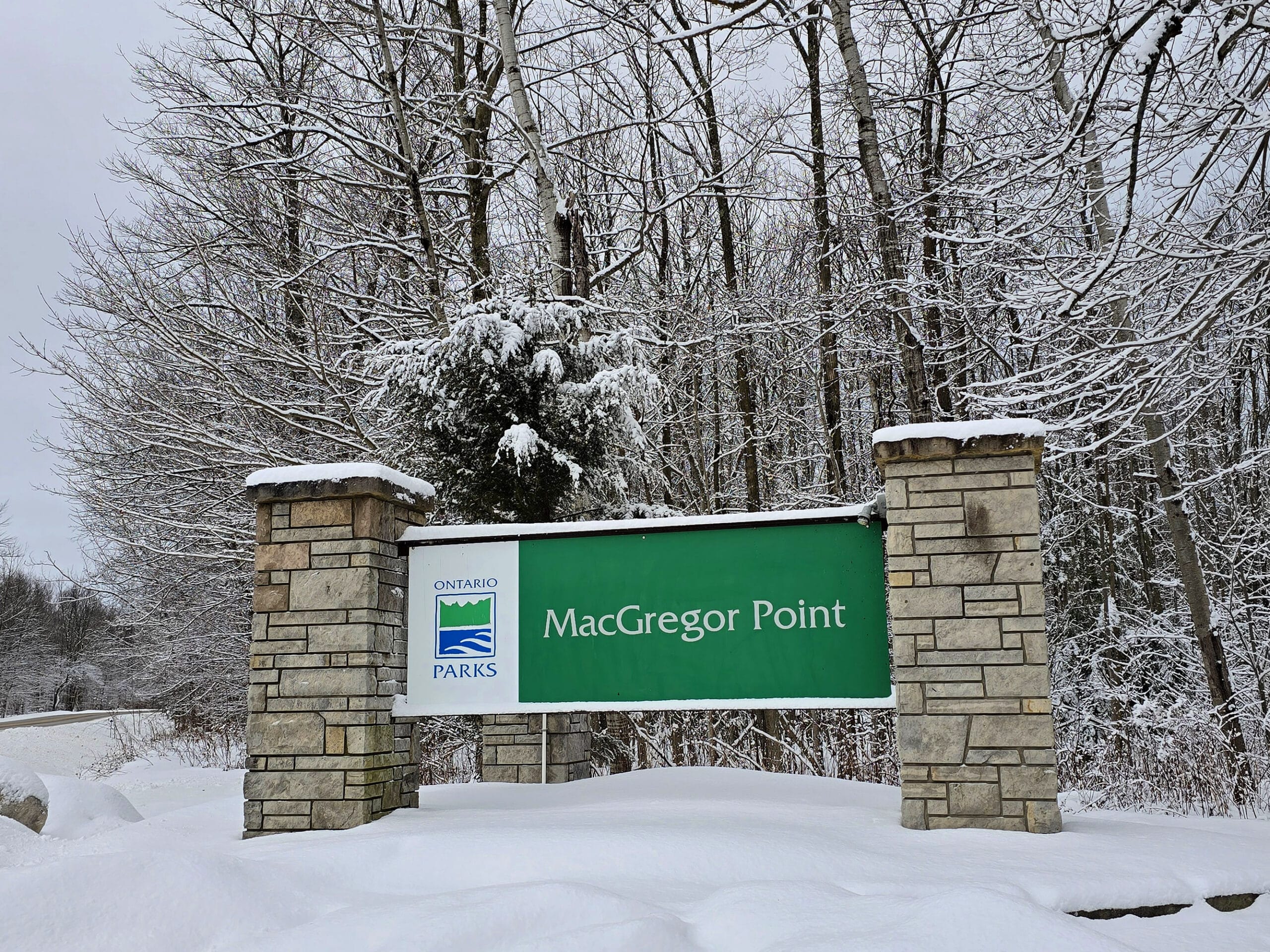 The MacGregor Point Provincial Park sign in winter, with snow covered trees behind it.