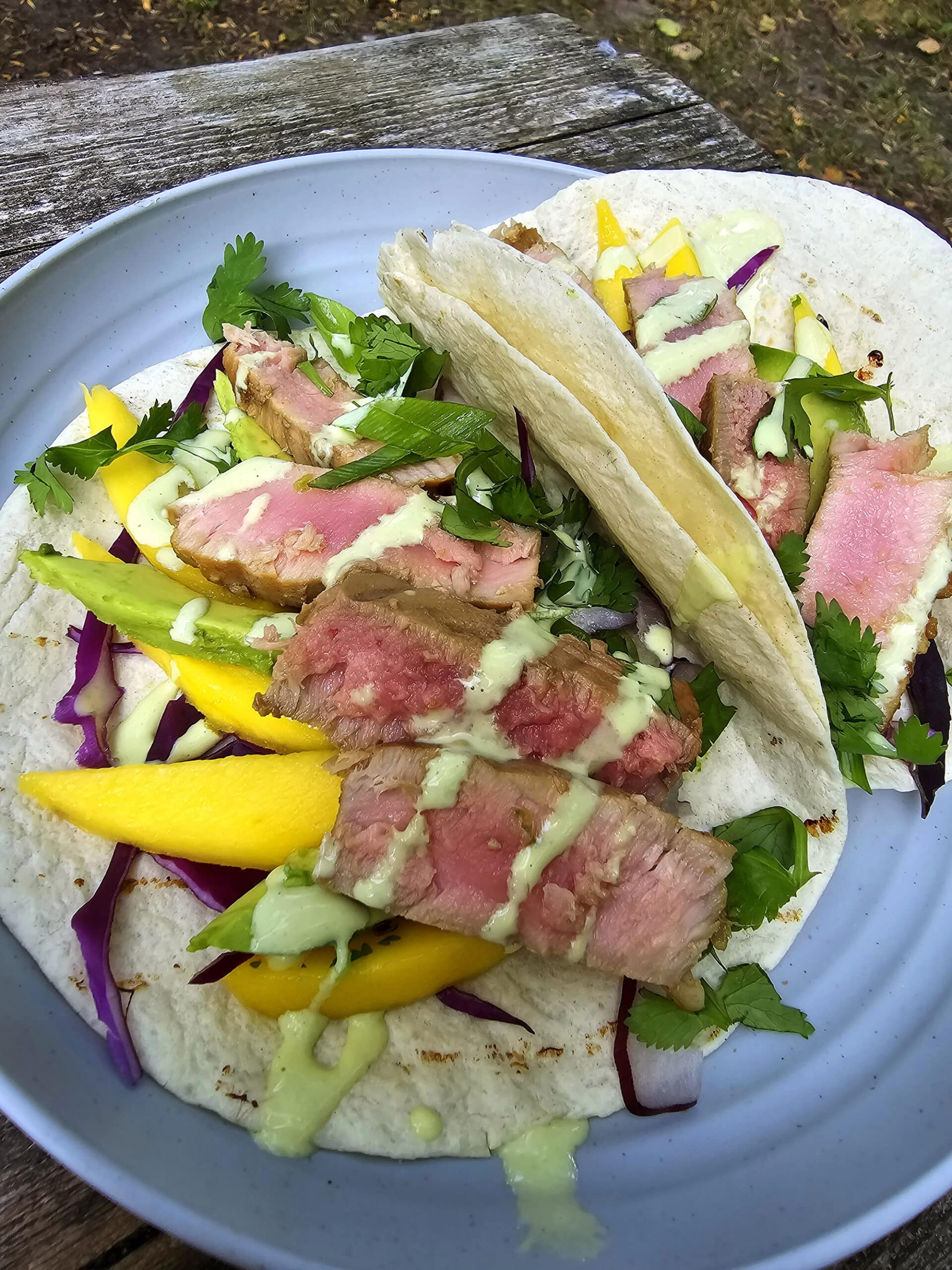 2 campfire grilled tuna tacos with mango slices, avocado, red cabbage, cilantro, and wasabi mayo on a plate.