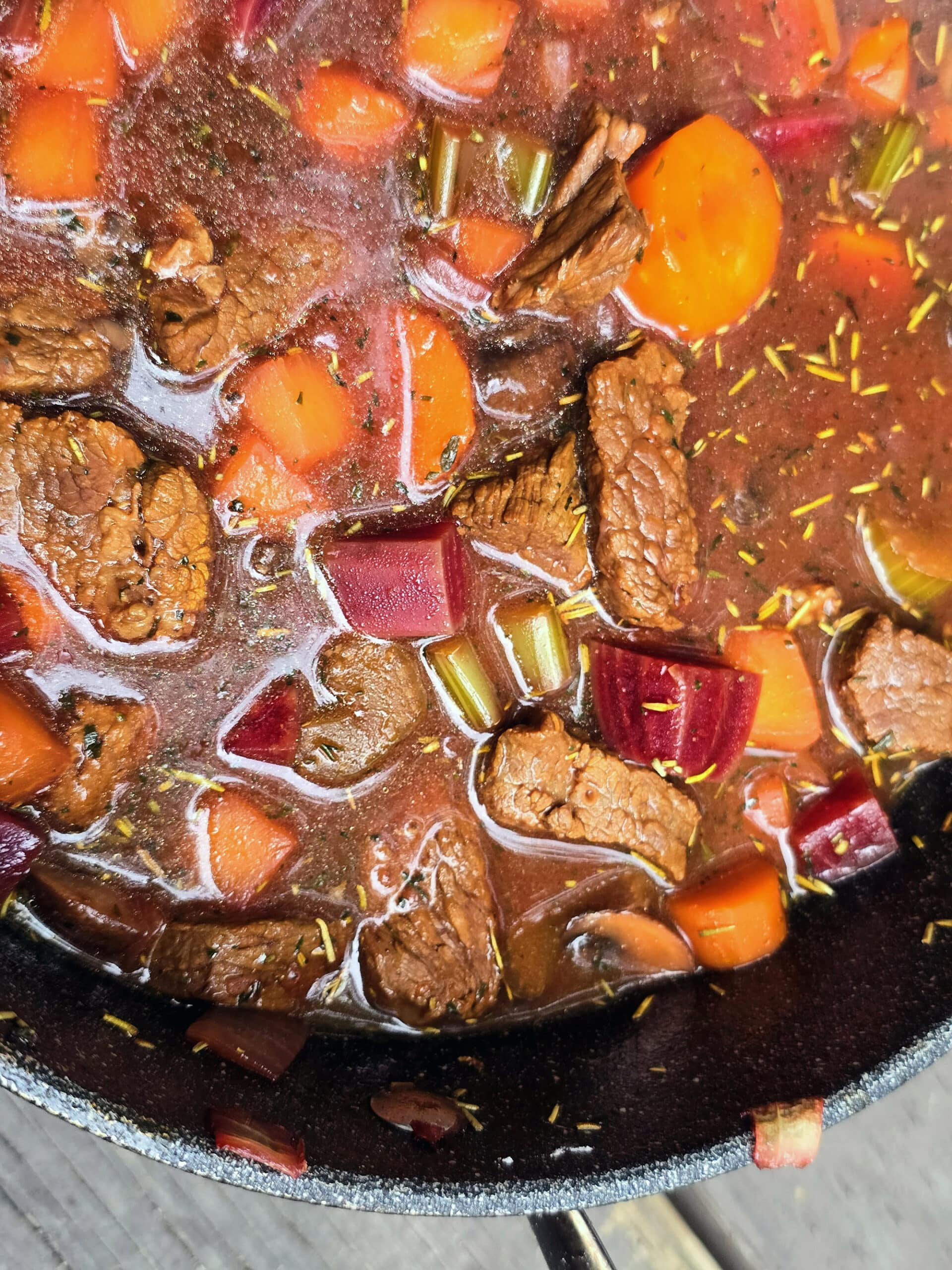 A pot of beef and root vegetable stew on a picnic table.