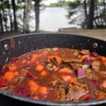 A pot of beef and root veggie stew on a picnic table.