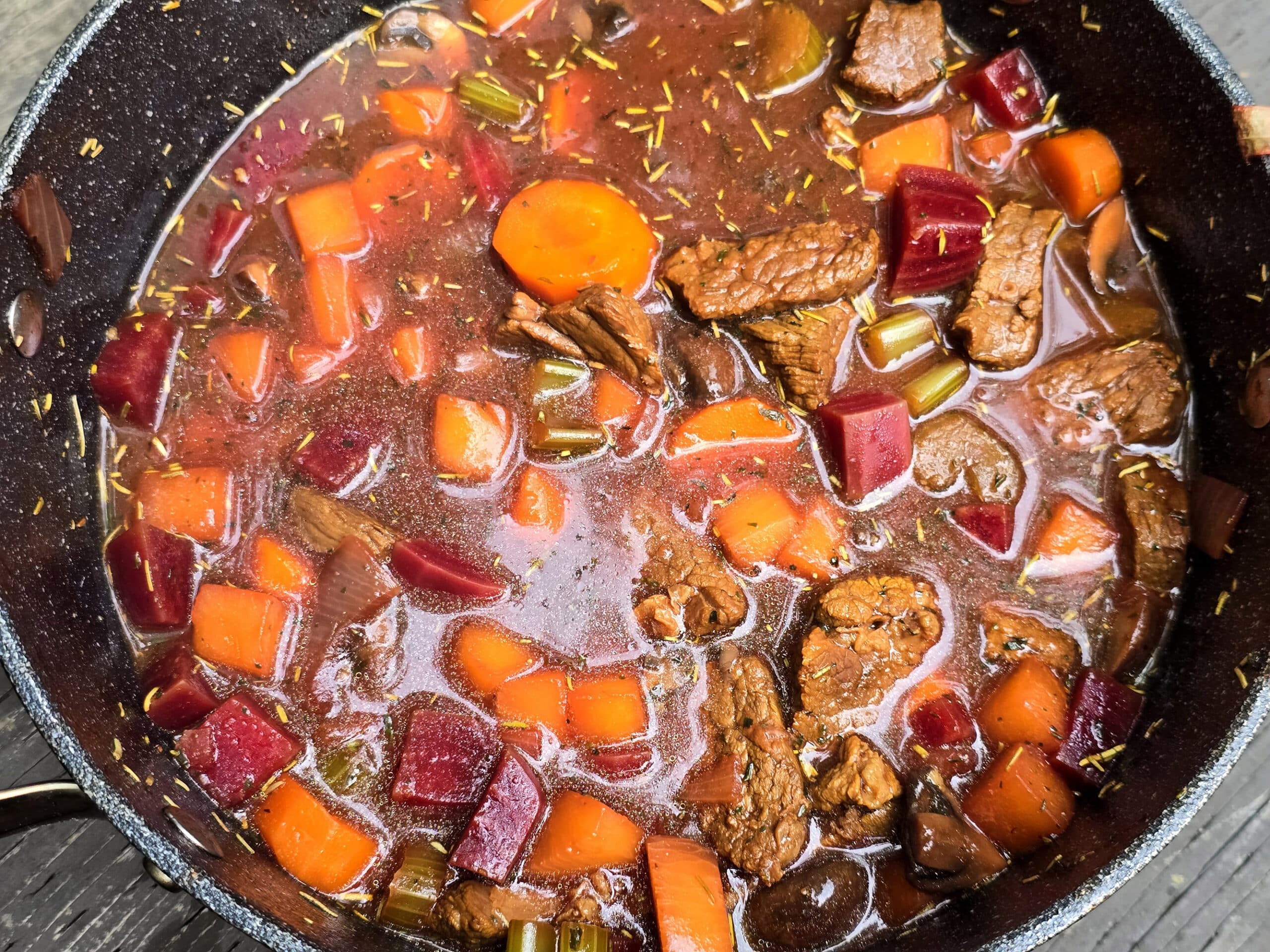 A pot of beef and root vegetable stew on a picnic table.