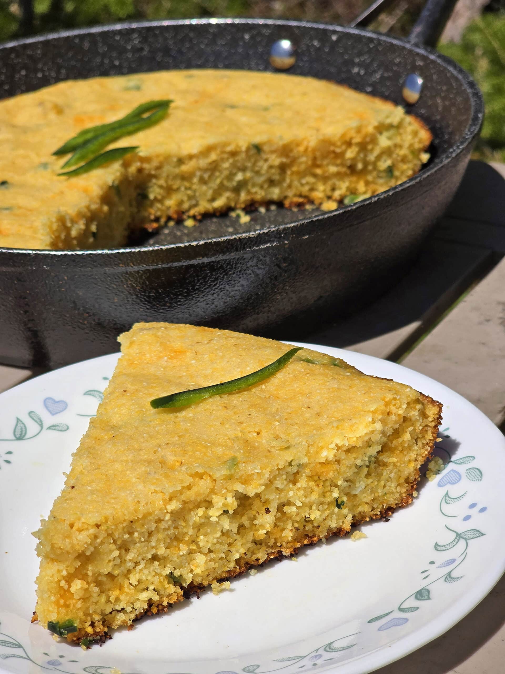 A pan of skillet jalapeno cheddar cornbread, with a slice on a plate.