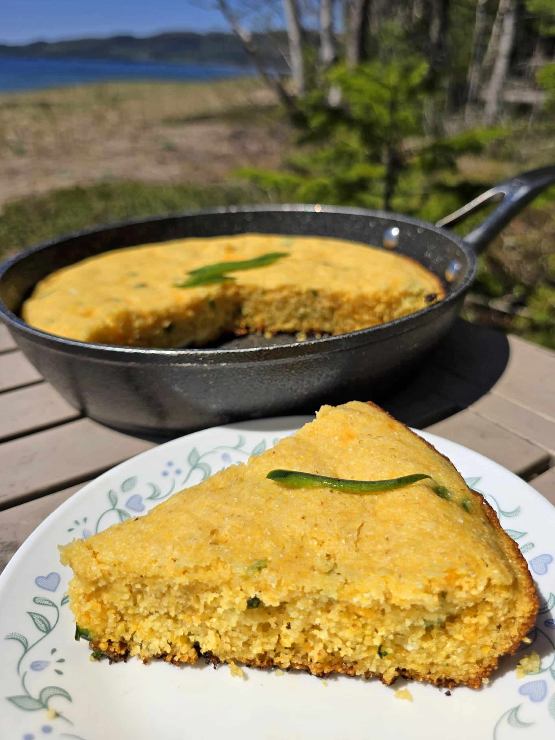 A pan of skillet cheddar jalapeno cornbread, with a slice on a plate.