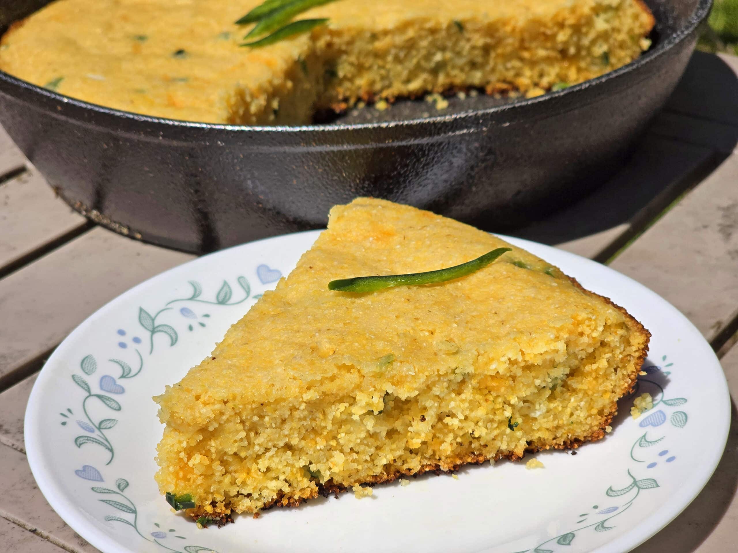 A pan of skillet jalapeno cheddar cornbread, with a slice on a plate.