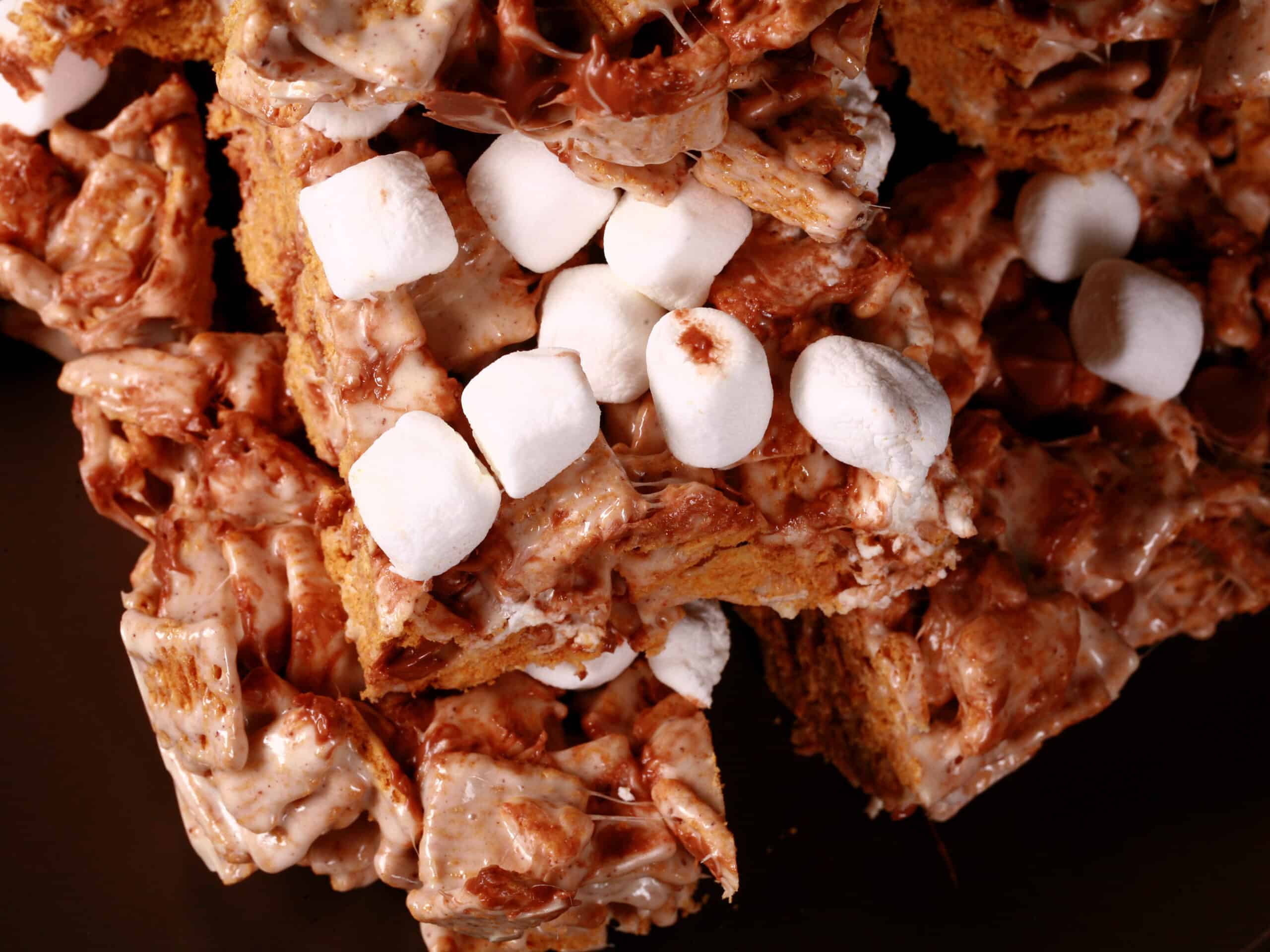 A plate of no-bake smores squares made with golden grahams cereal, melted marshmallows, mini marshmallows, browned butter, and chocolate chips.