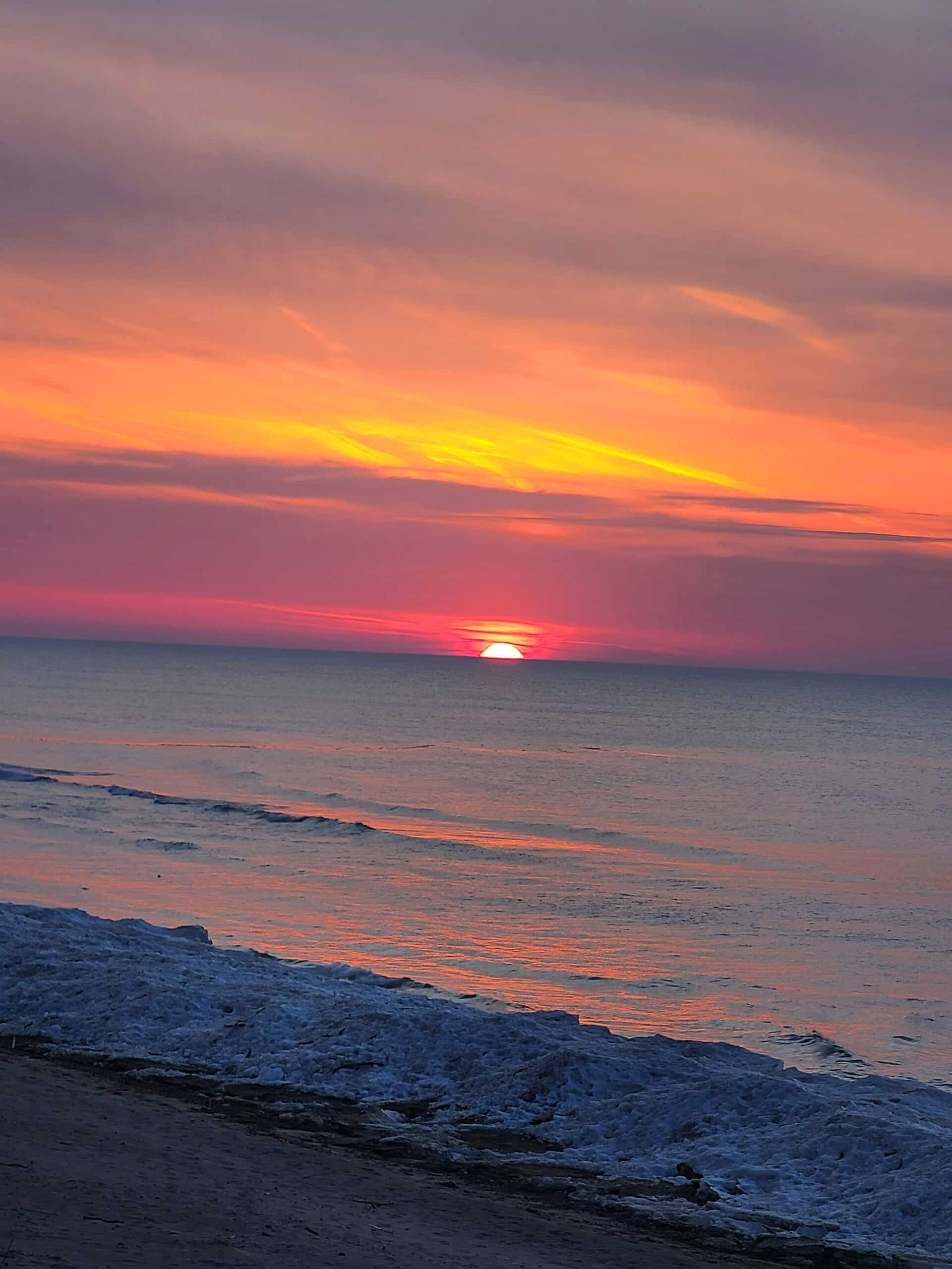 A pink and purple sunset over an icy lake huron shore.