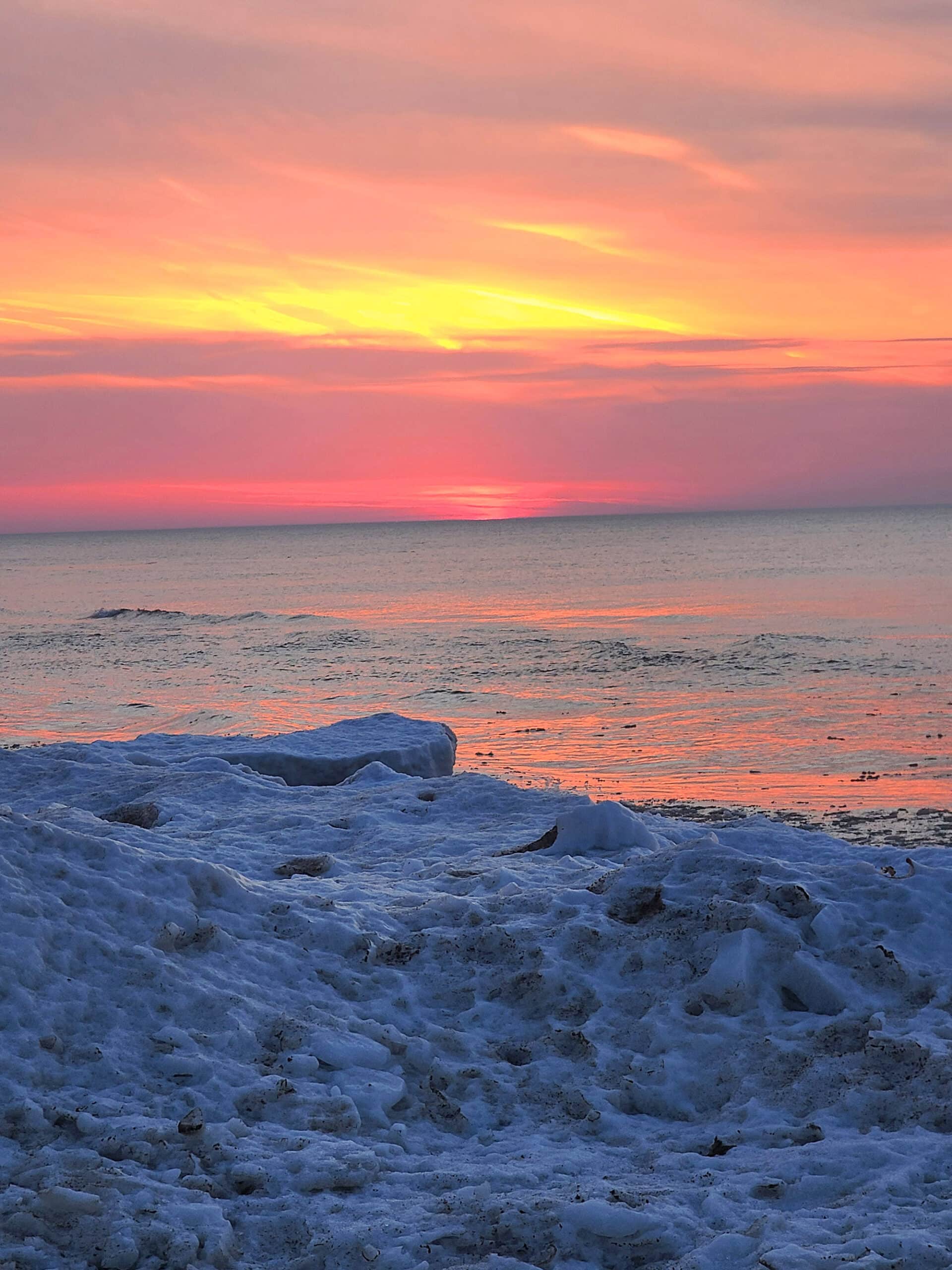 Sunset over lake huron, with an icy shore in the foreground.