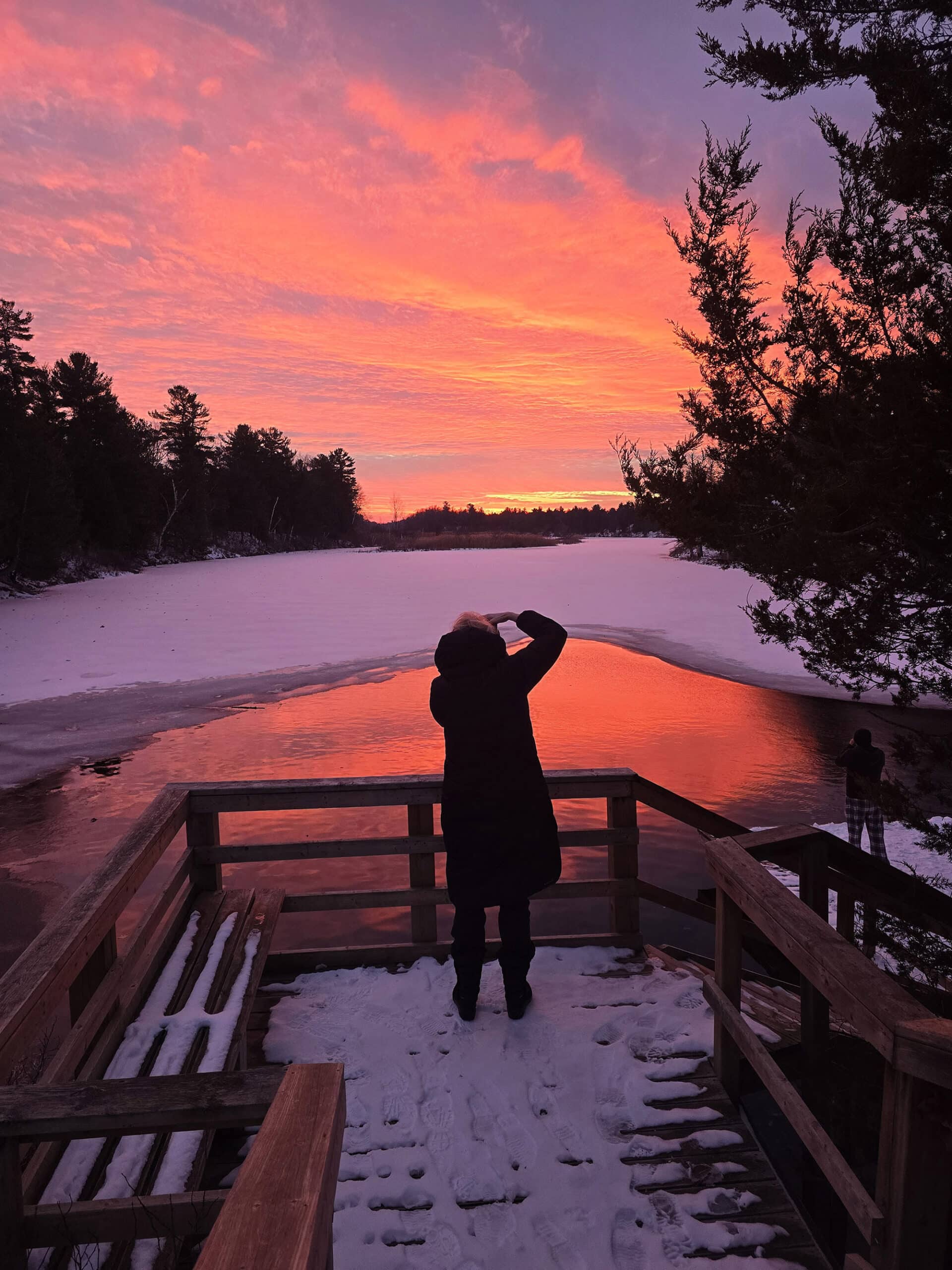 A woman standing in front of old ausable channel, taking a photo of the sunset.