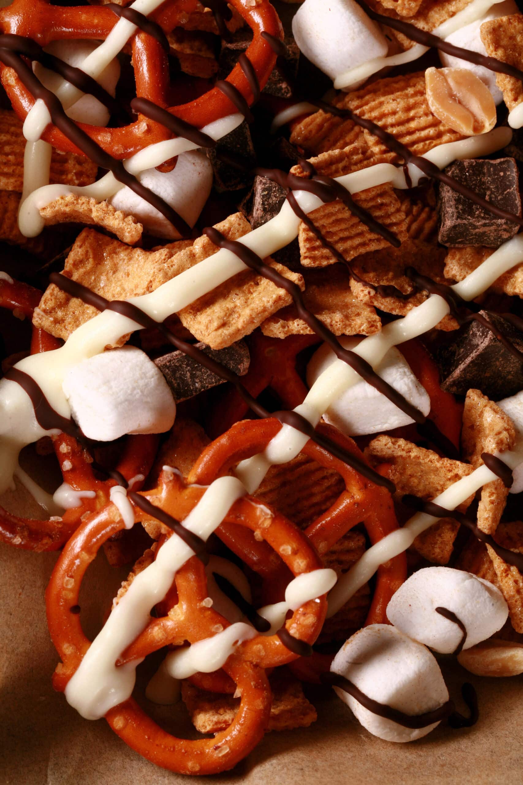 A pan of smores snack mix, with golden grahams cereal, chocolate chunks, peanuts, pretzels, and mini marshmallows, drizzled with white and milk chocolate.