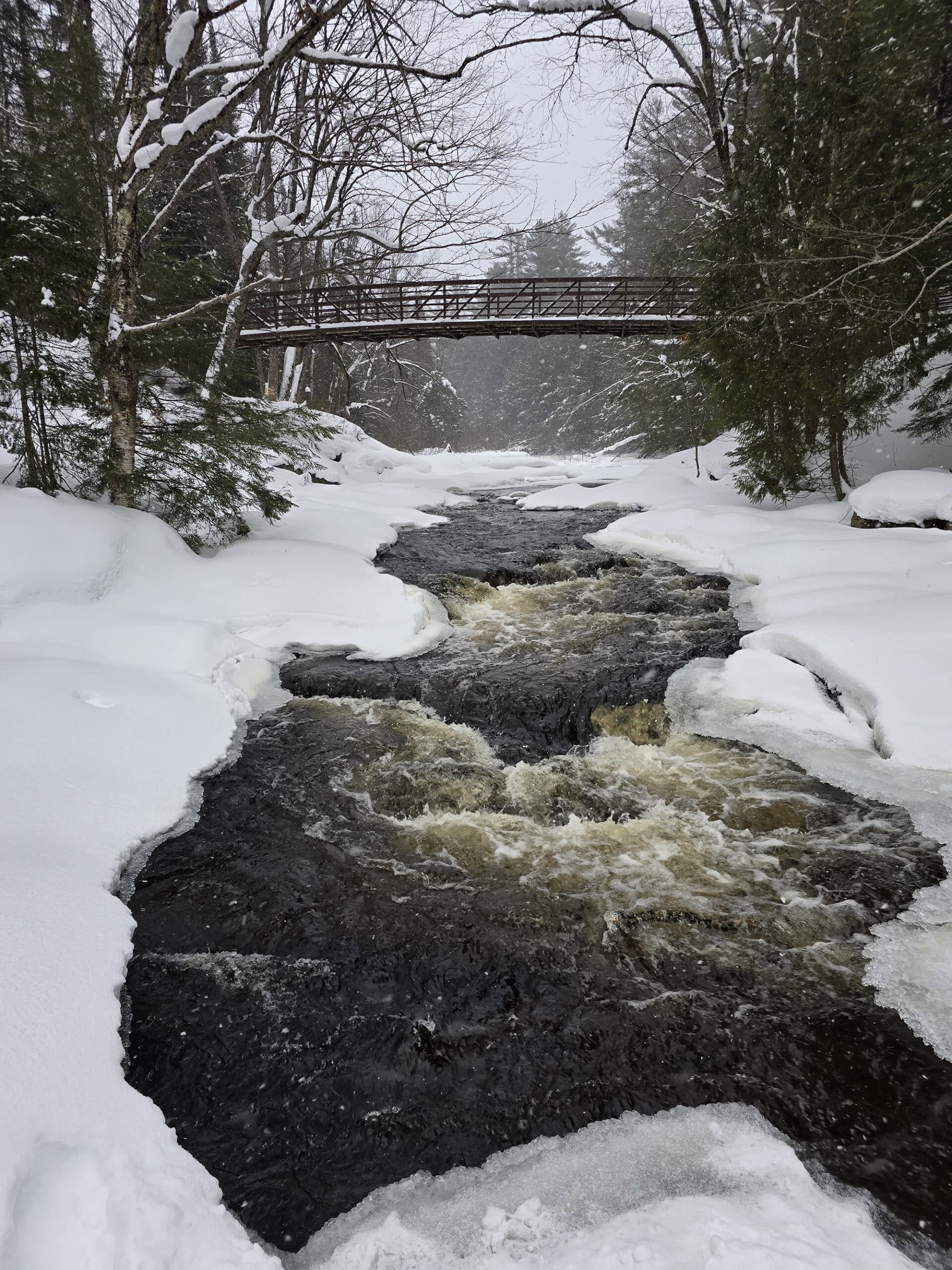 A river through the arrowhead provincial park woods in winter, with a bridge crossing it.