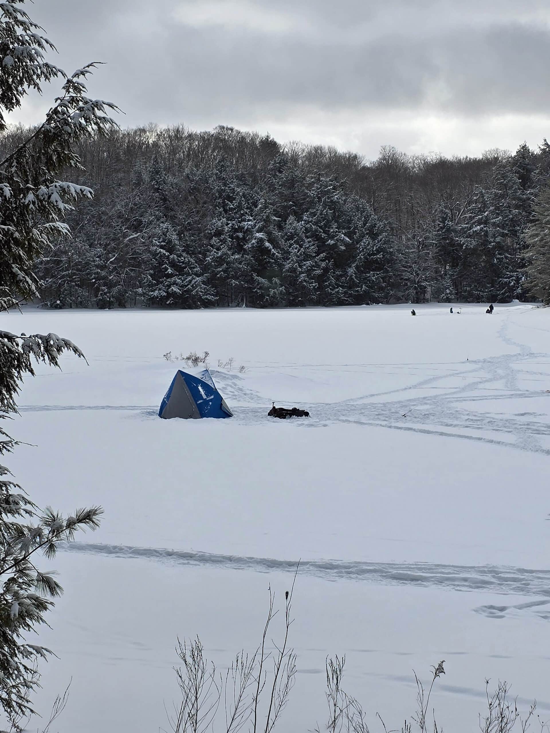 A tent and several people ice fishing on Mayflower Lake at Arrowhead Provincial Park.