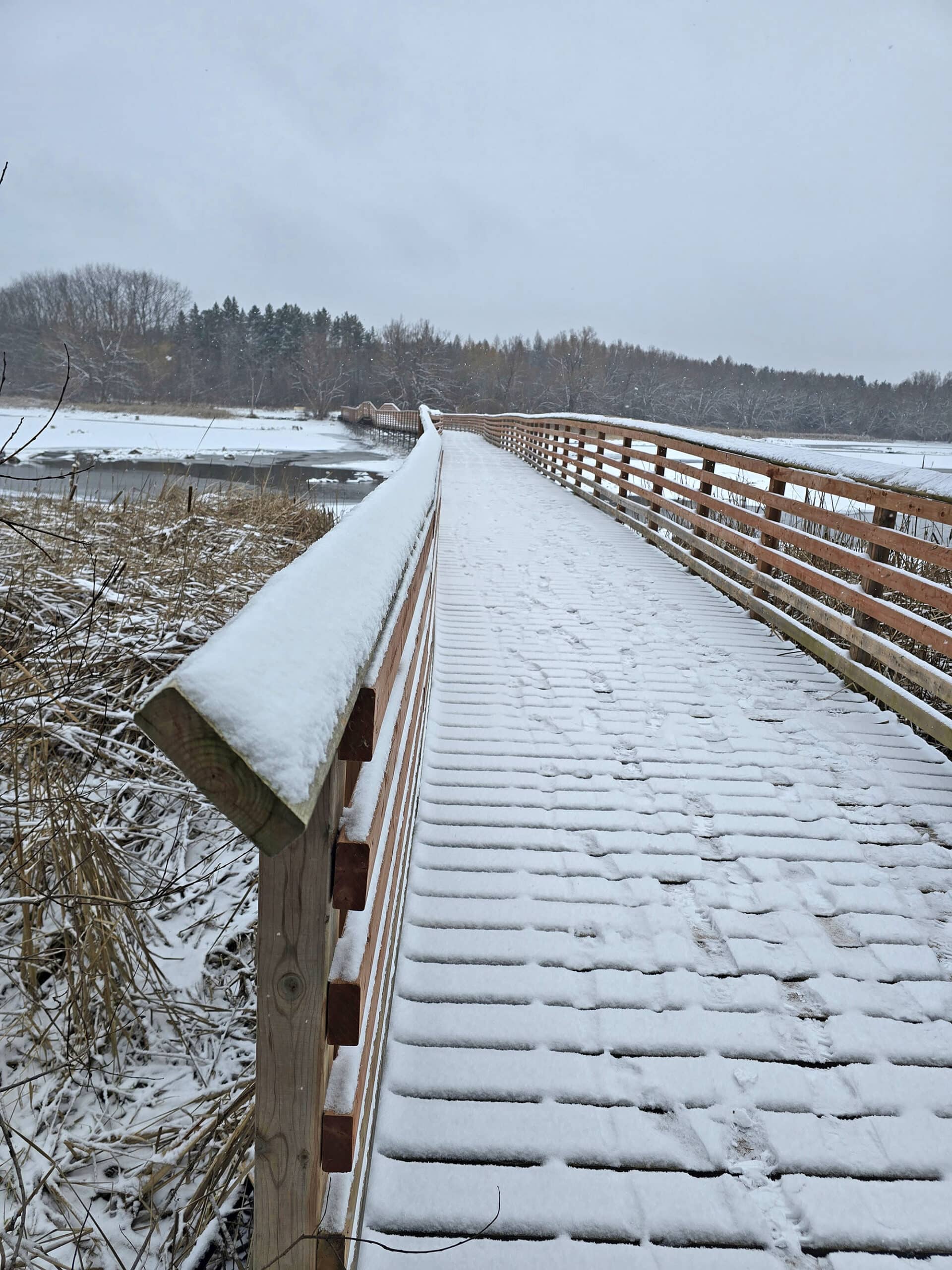 A snow covered wooden boardwalk going over a frozen valens lake.