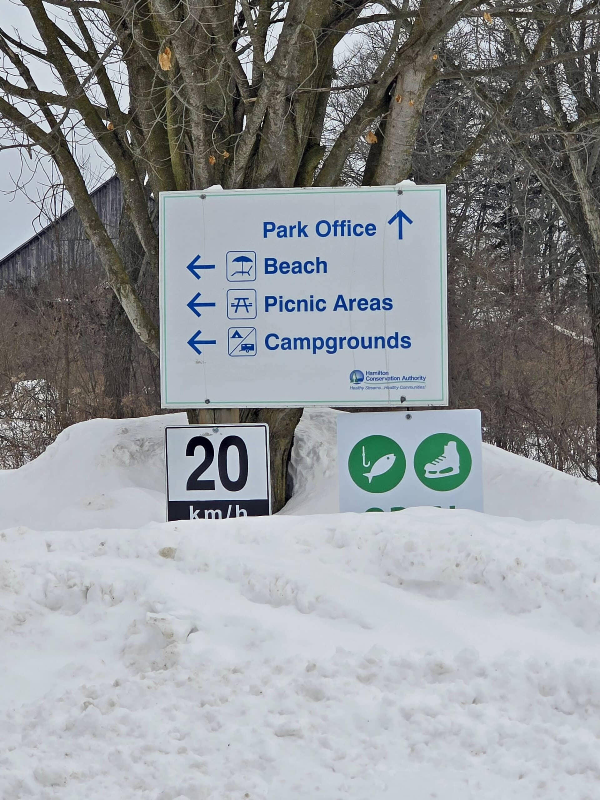 A directional road sign for Valens Lake Conservation Area, with snow pilled up and around it.