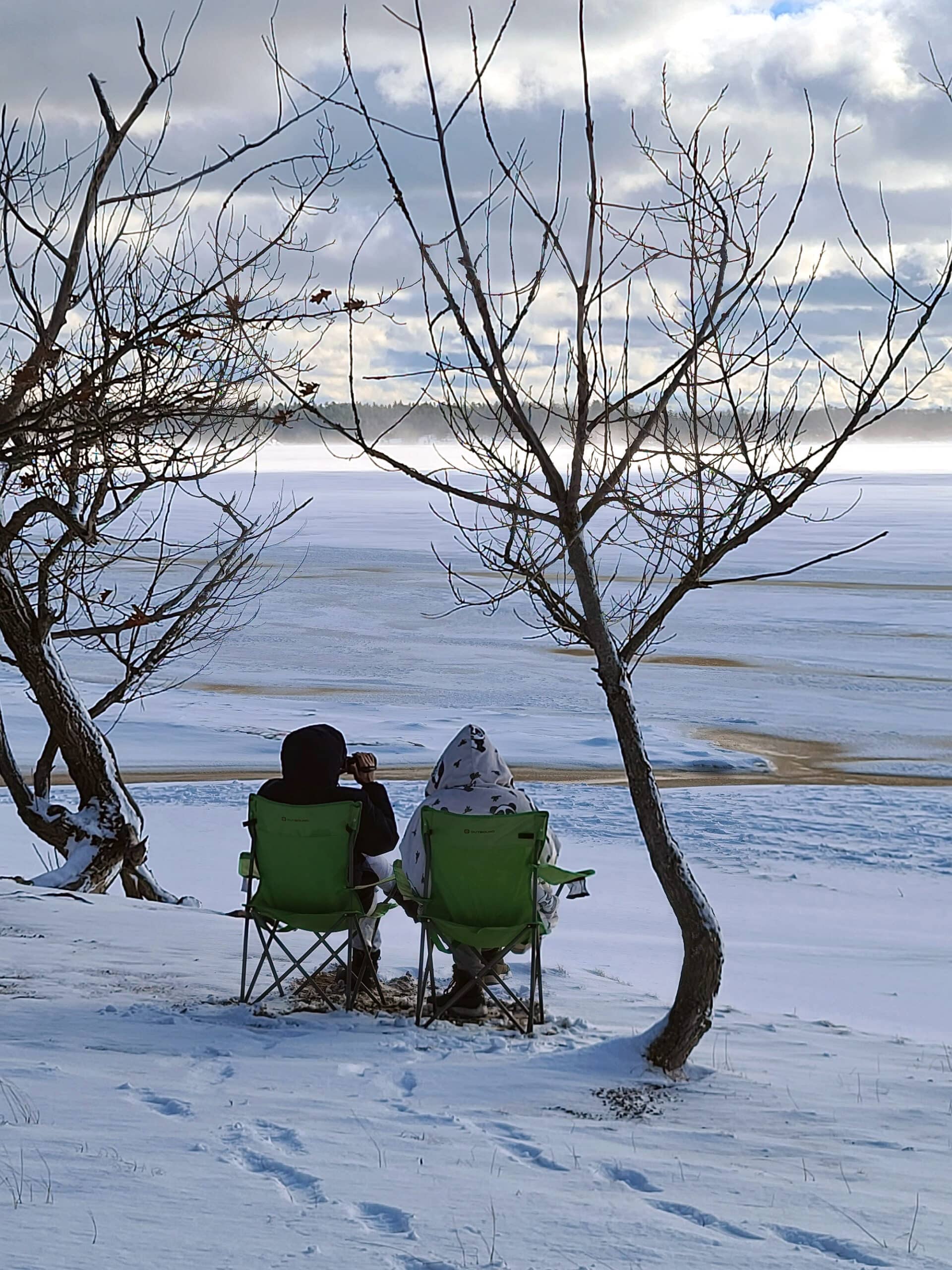 2 people sitting in lawn chairs on the snow watching sunset over a frozen Georgian Bay at Killbear Provincial Park.