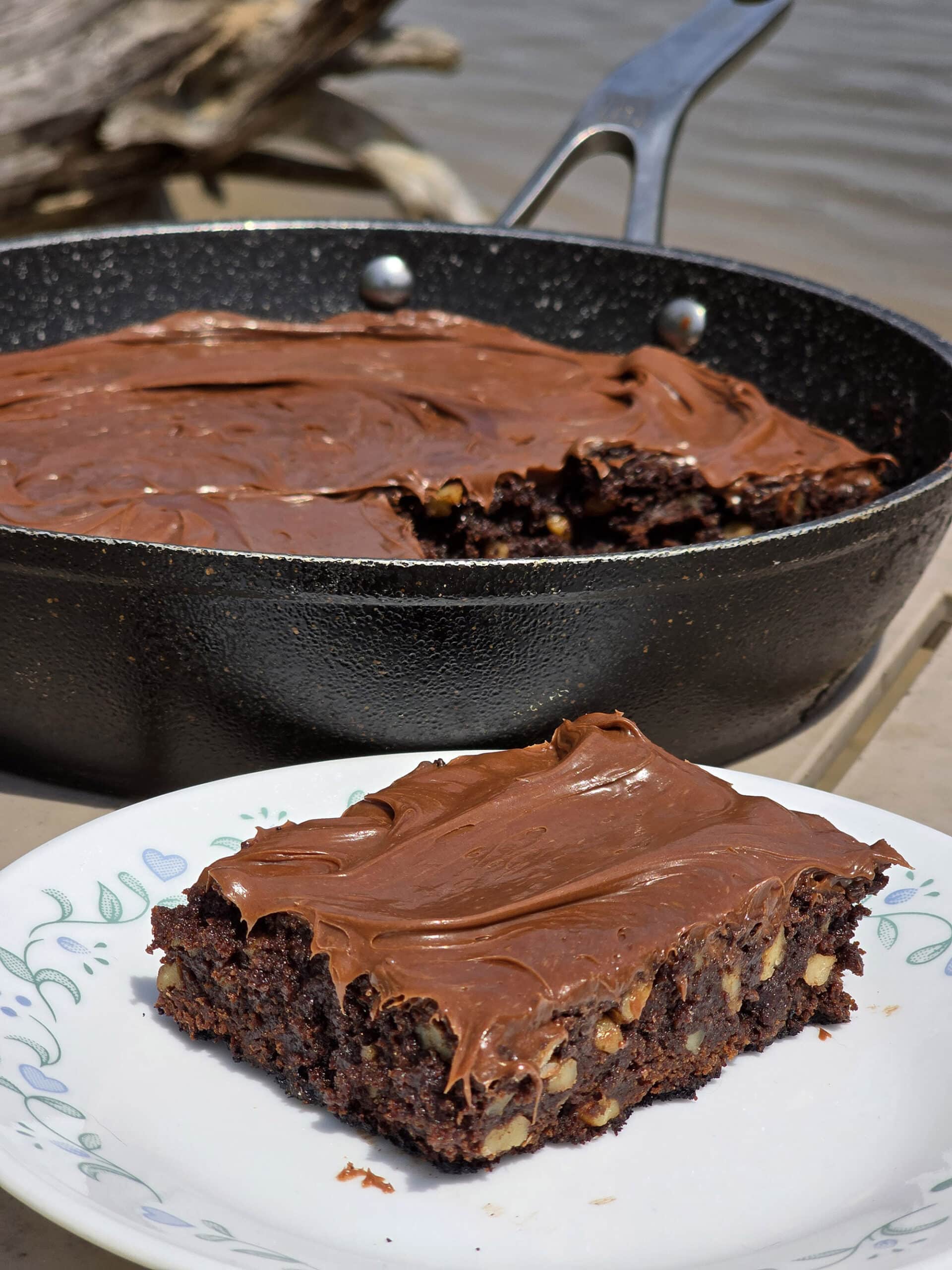 A pan of skillet campfire brownies on a picnic table, with a single brownie on a plate in front of it.