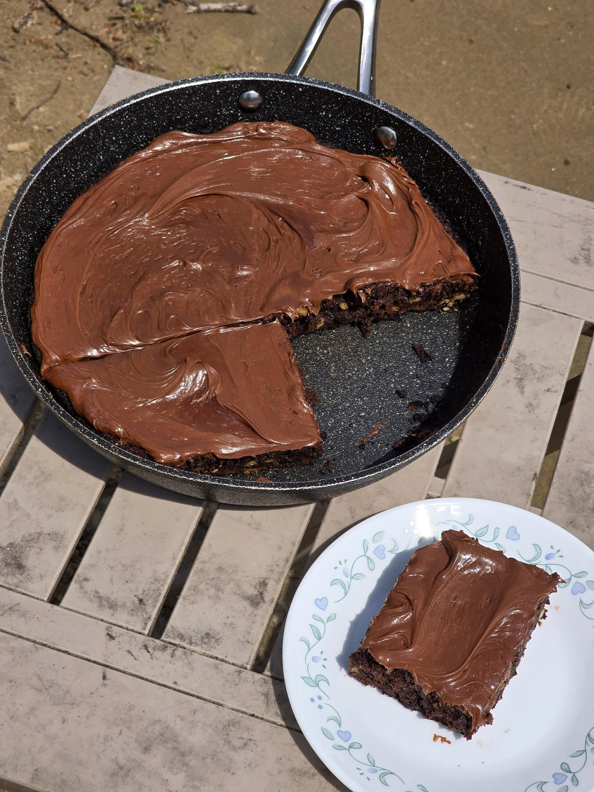 A pan of skillet brownies on a picnic table, with a single brownie on a plate in front of it.