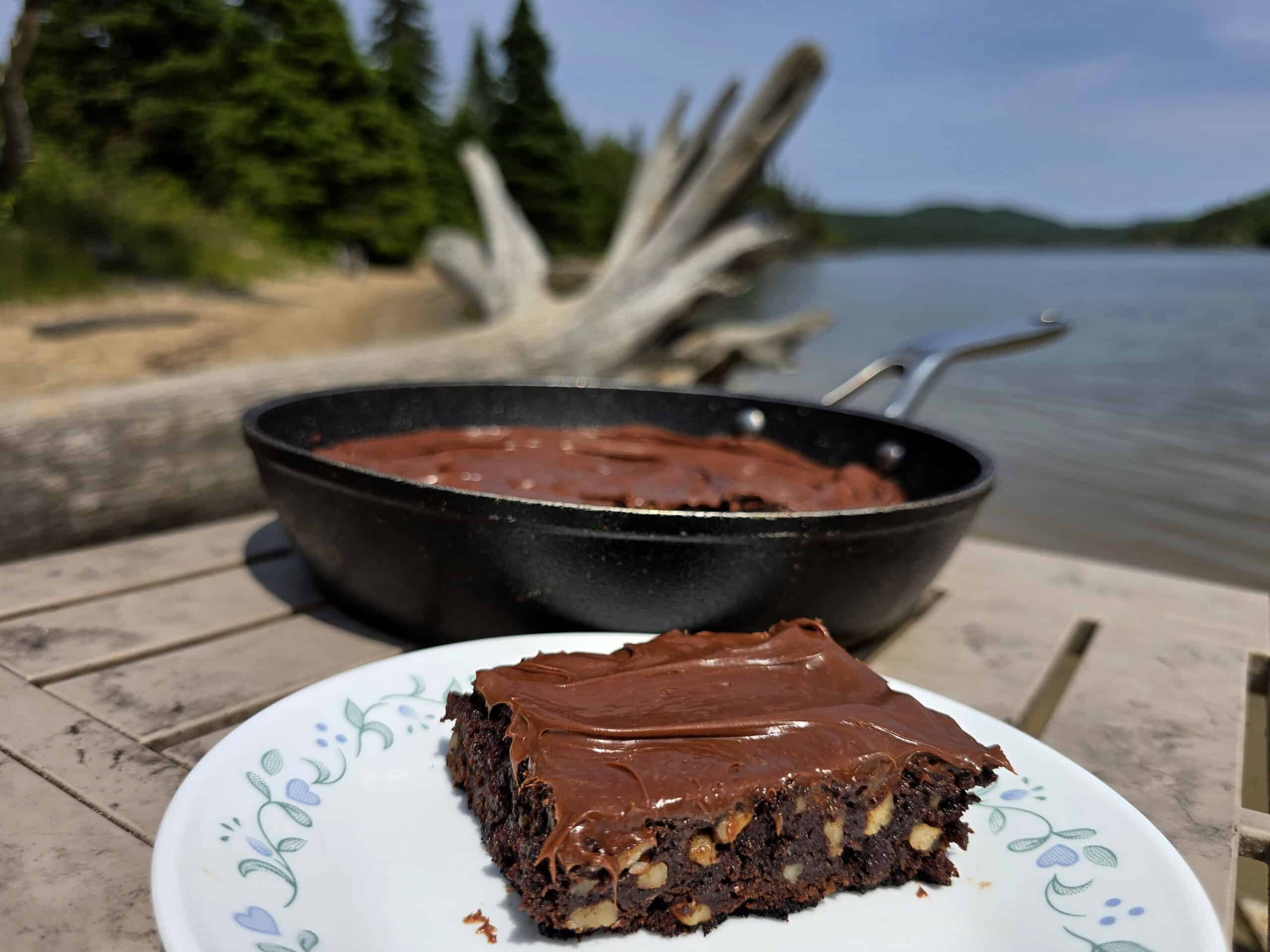 A pan of skillet brownies on a picnic table, with a single brownie on a plate in front of it.