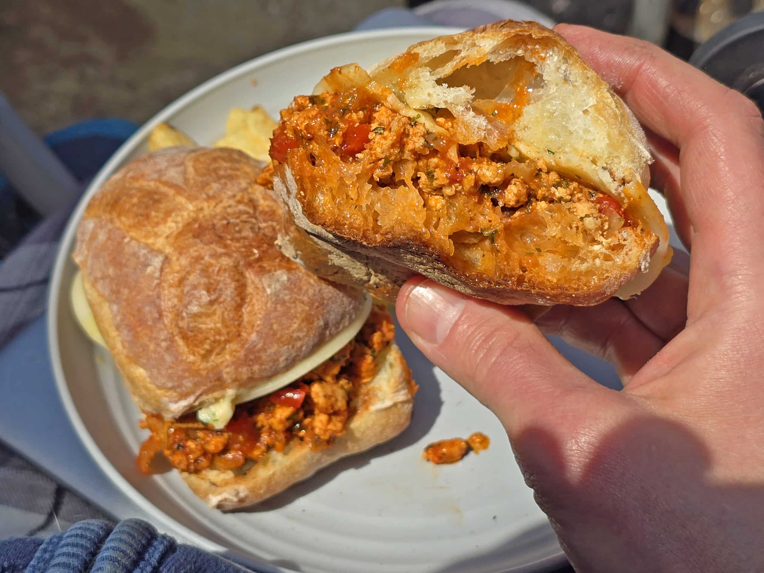Two Sloppy Giuseppes - ciabatta rolls, seasoned meat filling, provolone cheese, and garlic butter - on a plate resting on a picnic table.