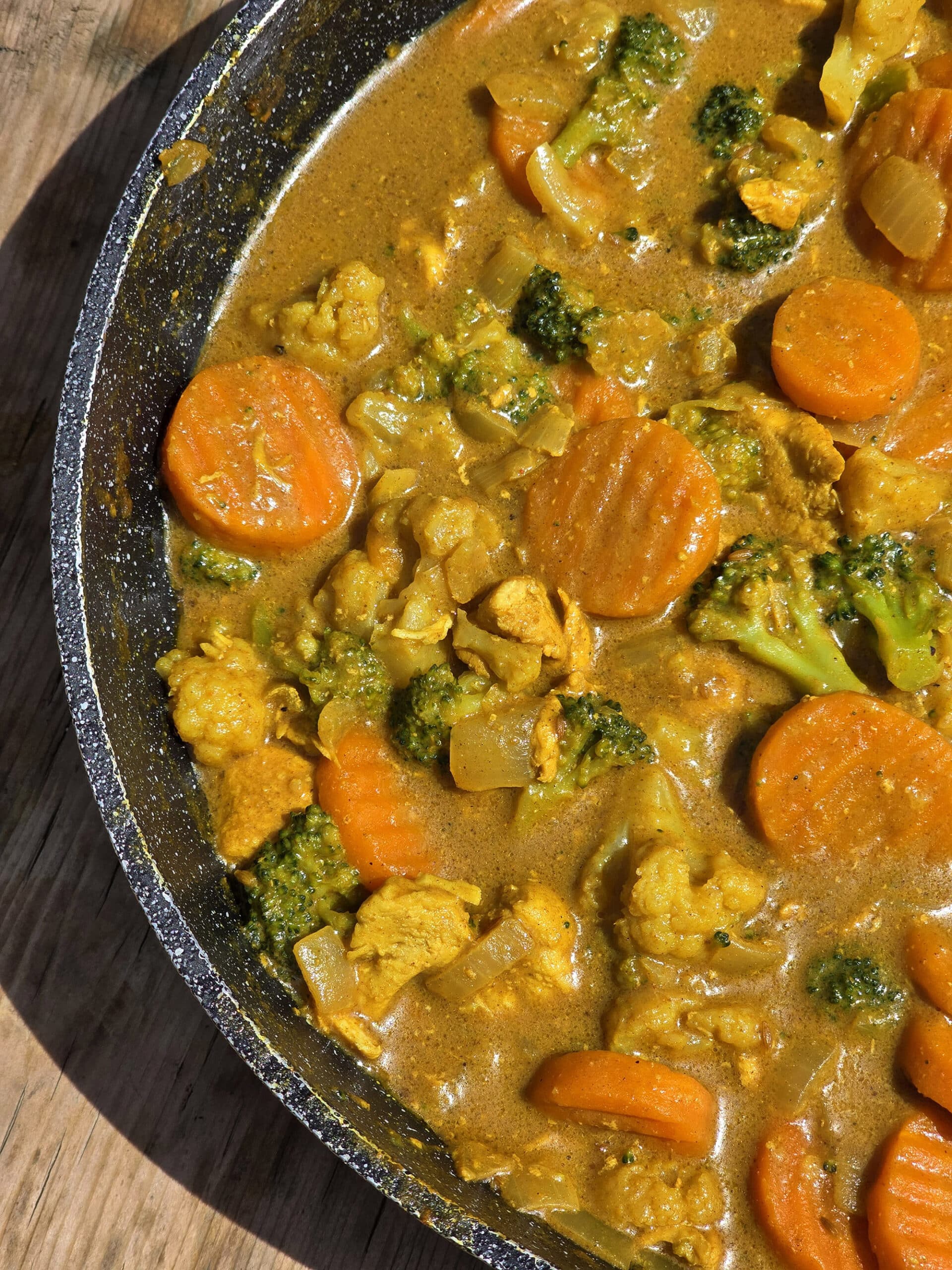 A pan of campfire chicken curry with broccoli, carrots, and cauliflower in a yellow sauce.