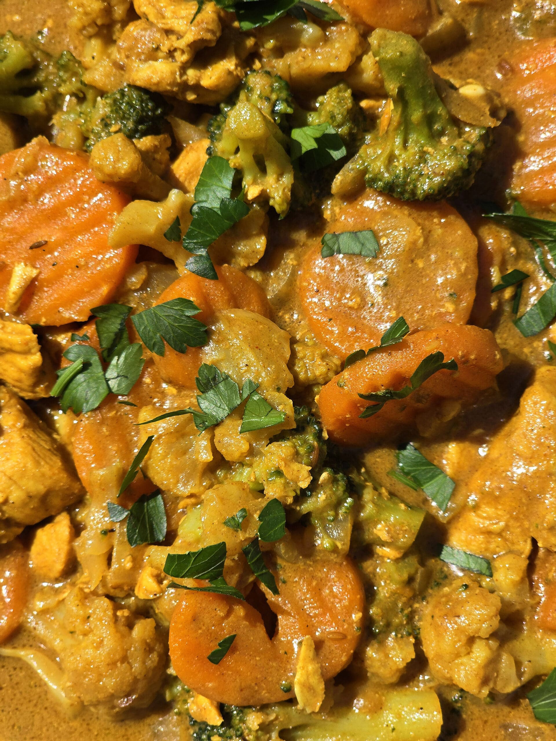 A pan of campfire chicken curry with broccoli, carrots, and cauliflower in a yellow sauce.