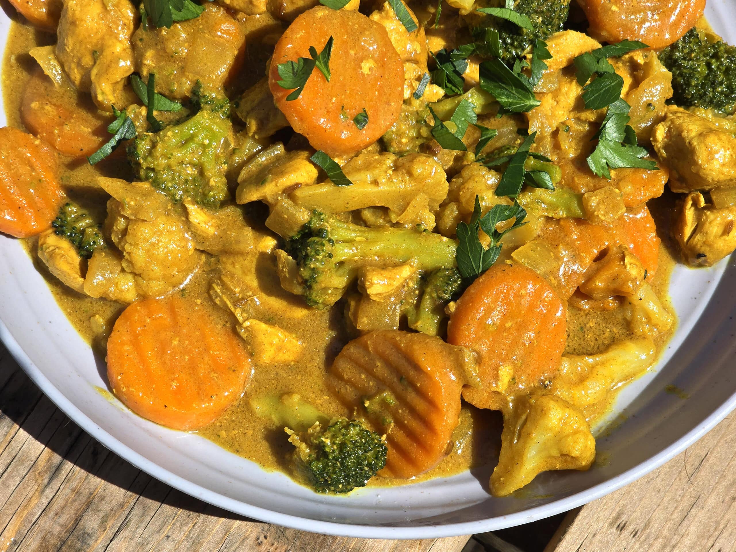 A bowl of campfire chicken curry with broccoli, carrots, and cauliflower in a yellow sauce.