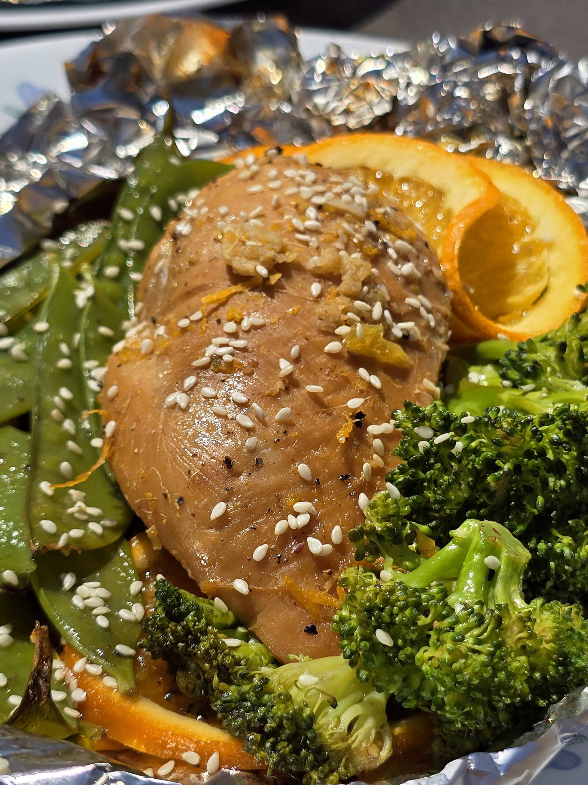 2 portions of orange ginger chicken in foil packets, with broccoli and peas.