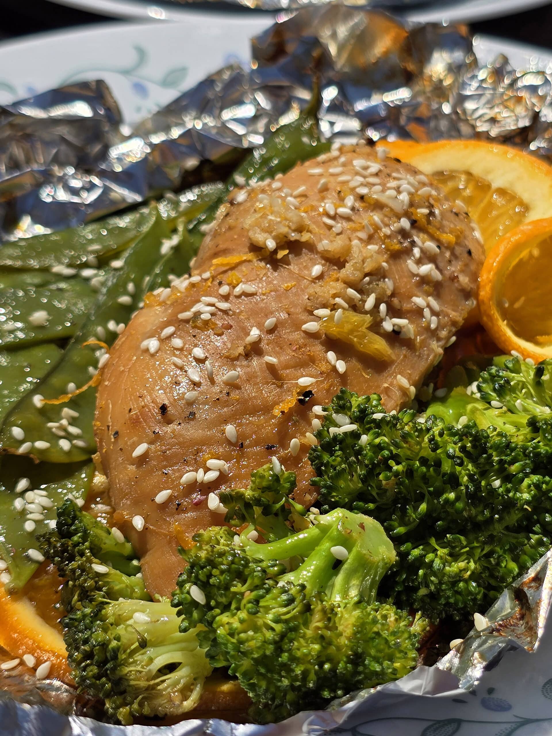 2 portions of orange ginger chicken in foil packets, with broccoli and peas.