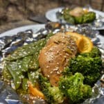 2 portions of orange ginger chicken in foil packets, with broccoli and peas.