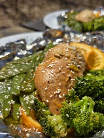 2 portions of orange ginger chicken in foil packets, with broccoli and peas.