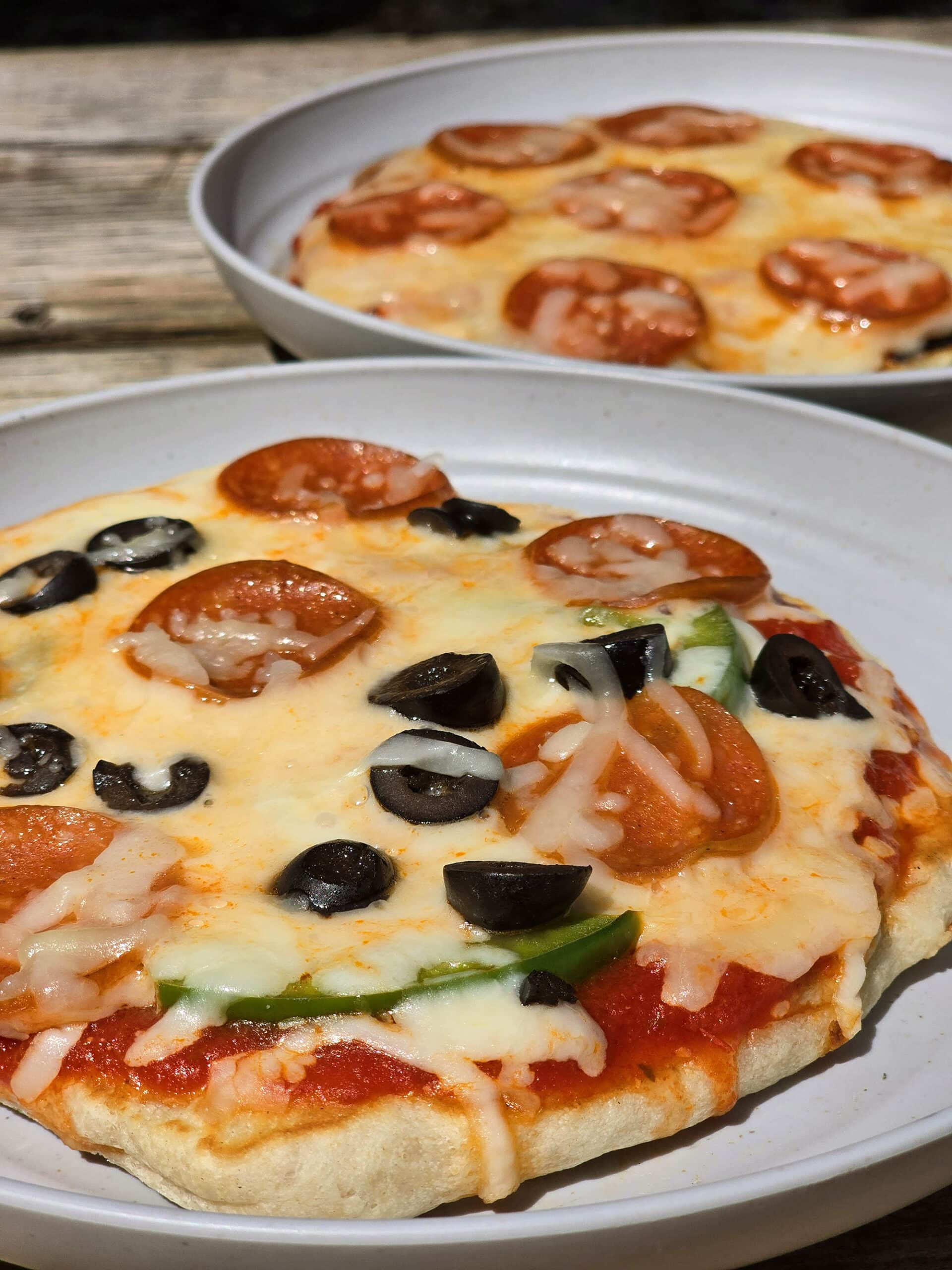 Two individual campfire pizzas, each on a plate.