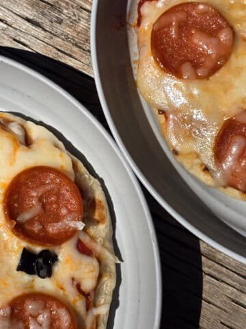 Two individual campfire pizzas, each on a plate.