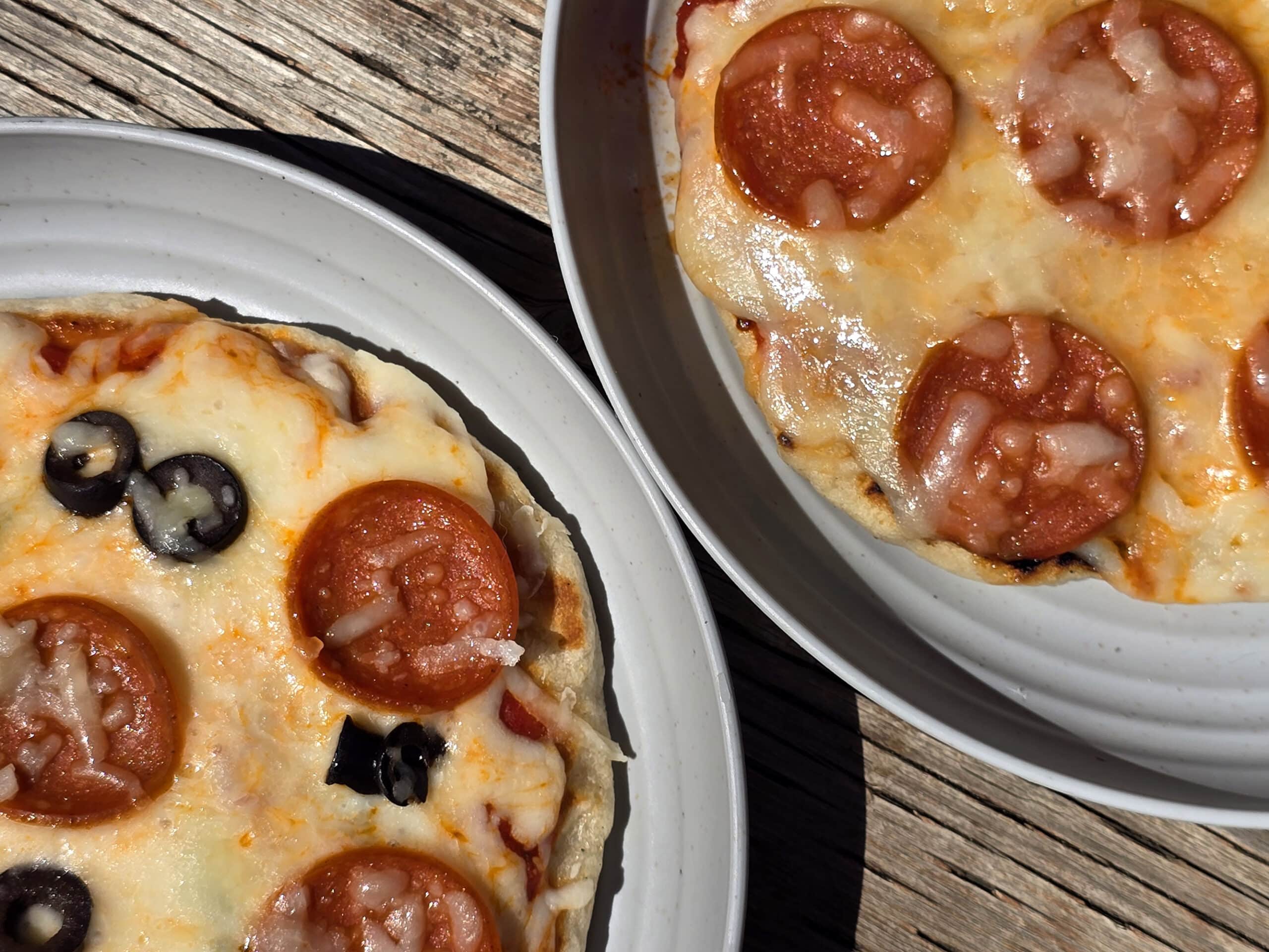Two individual campfire pizzas, each on a plate.
