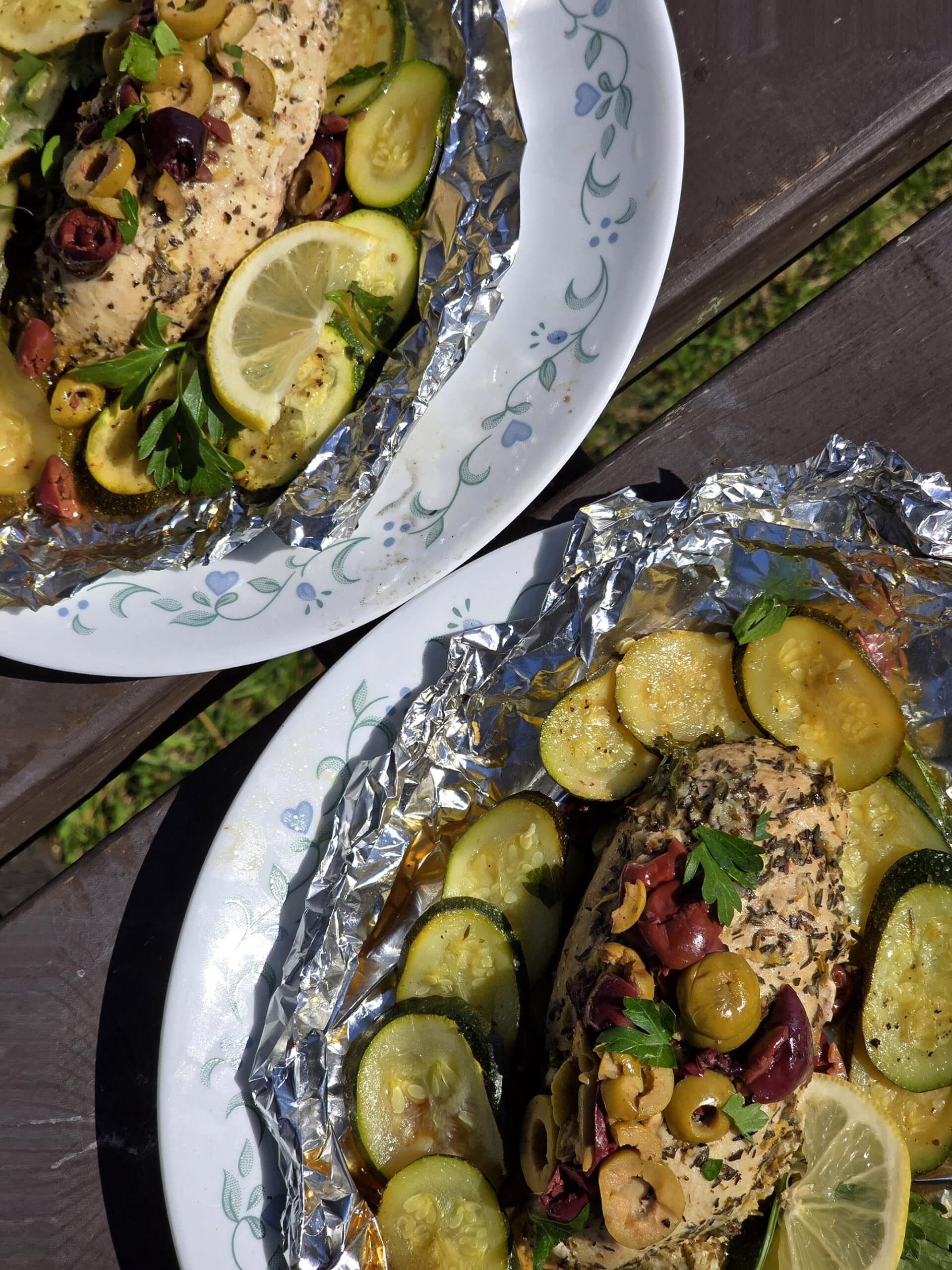Mediterranean foil packet chicken with souvlaki chicken breasts, lemon slices, grilled zucchini, parsley, and olives.