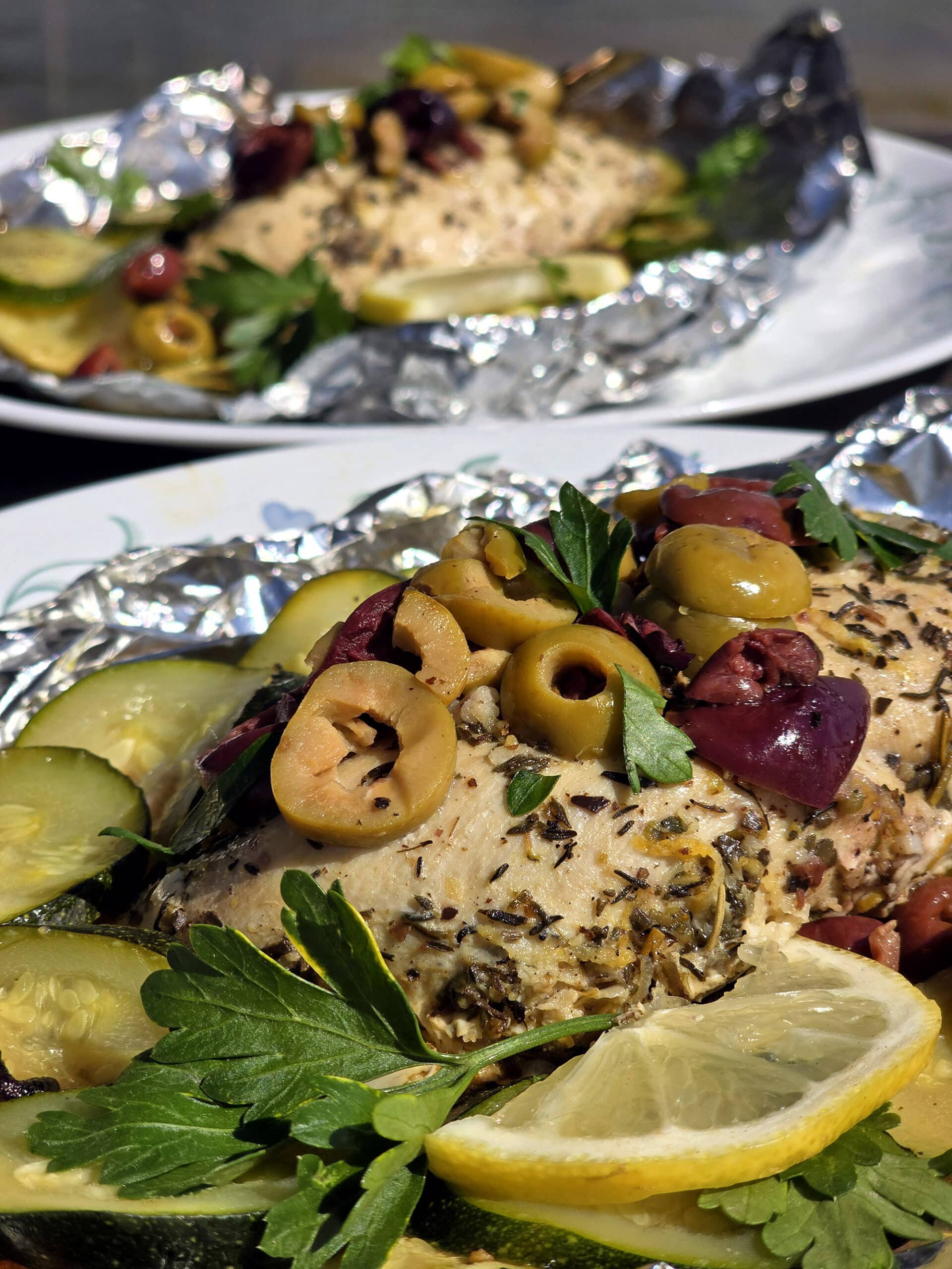 Mediterranean foil packet chicken with souvlaki chicken breasts, lemon slices, grilled zucchini, parsley, and olives.