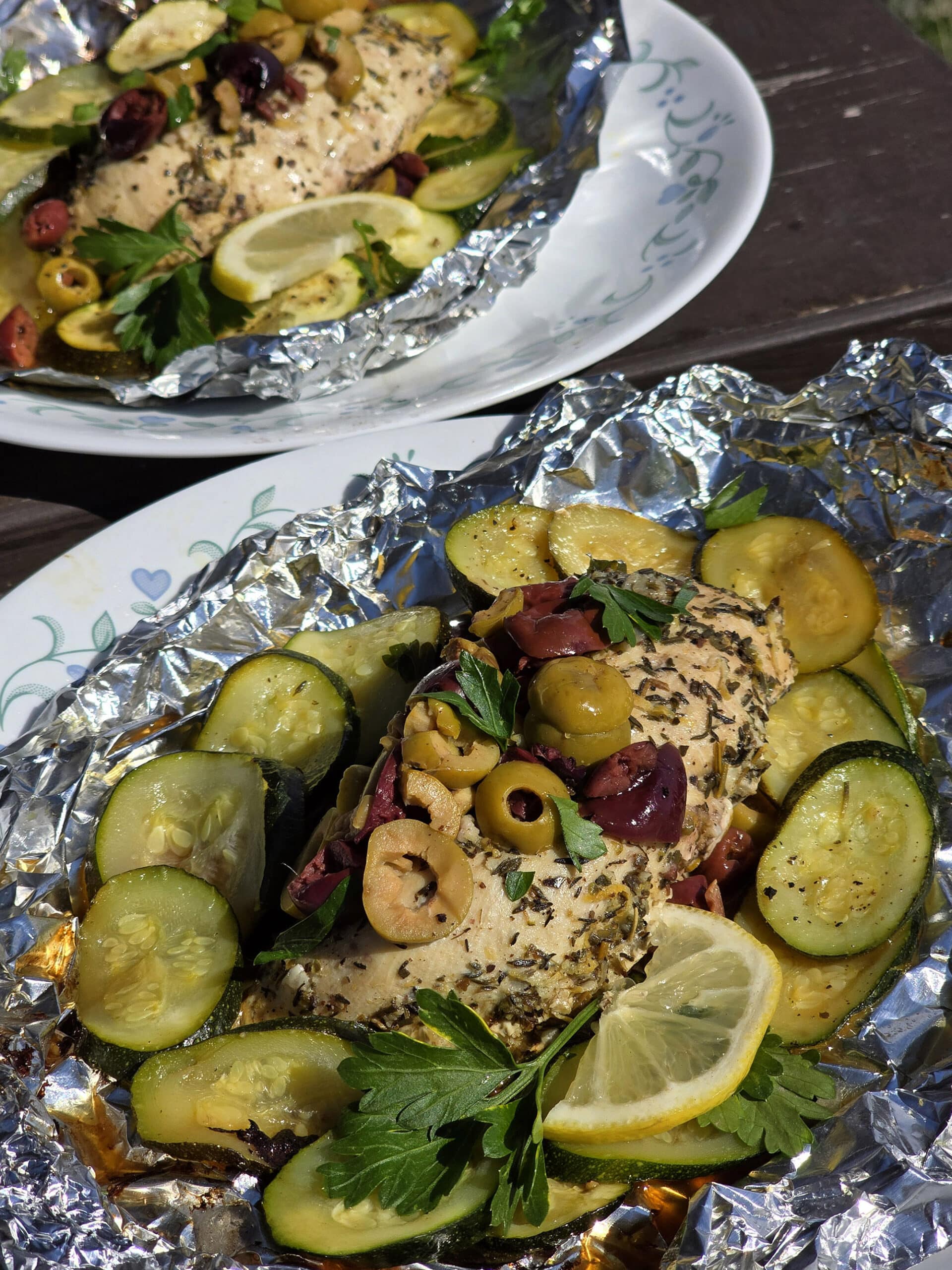 Mediterranean foil packet chicken with souvlaki chicken breasts, lemon slices, grilled zucchini, parsley, and olives.