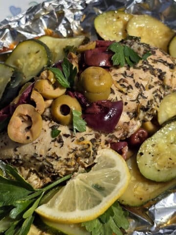 Souvlaki chicken foil packets with lemon slices, grilled zucchini, parsley, and olives.