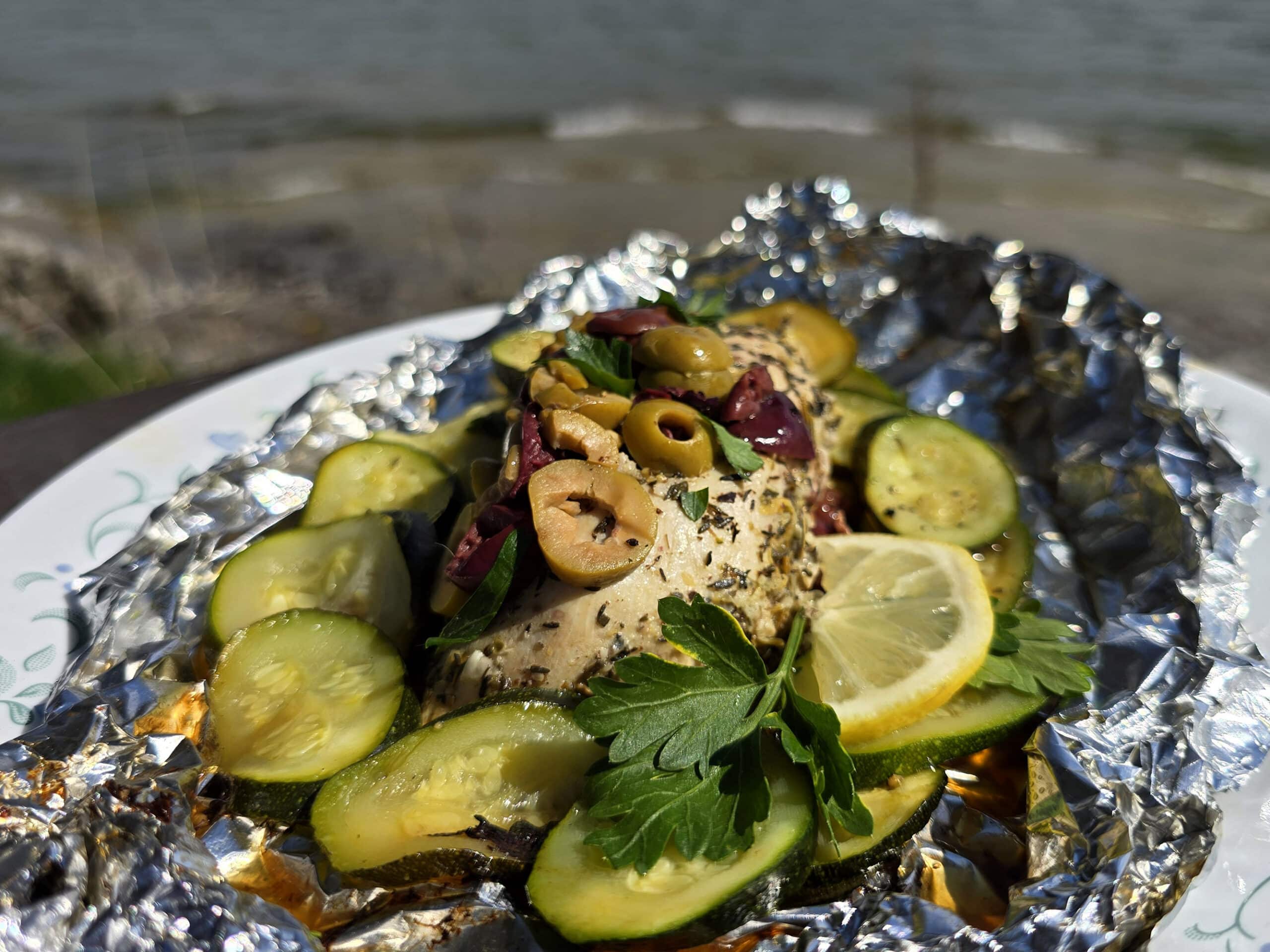 Mediterranean foil packet chicken with souvlaki chicken breasts, lemon slices, grilled zucchini, parsley, and olives.