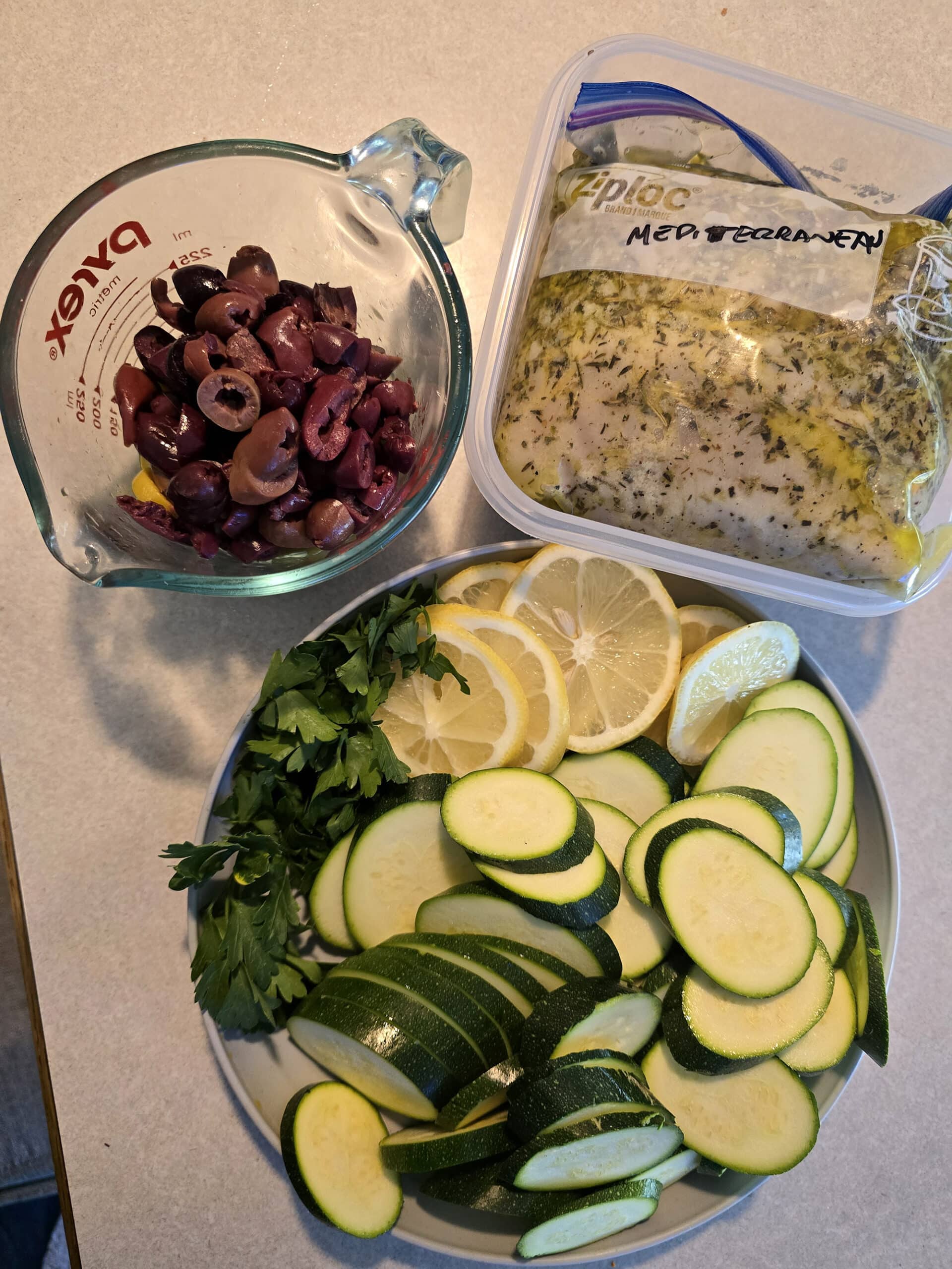 Olives, marinated chicken, and a plate with zucchini slices, lemon slices, and parsley.