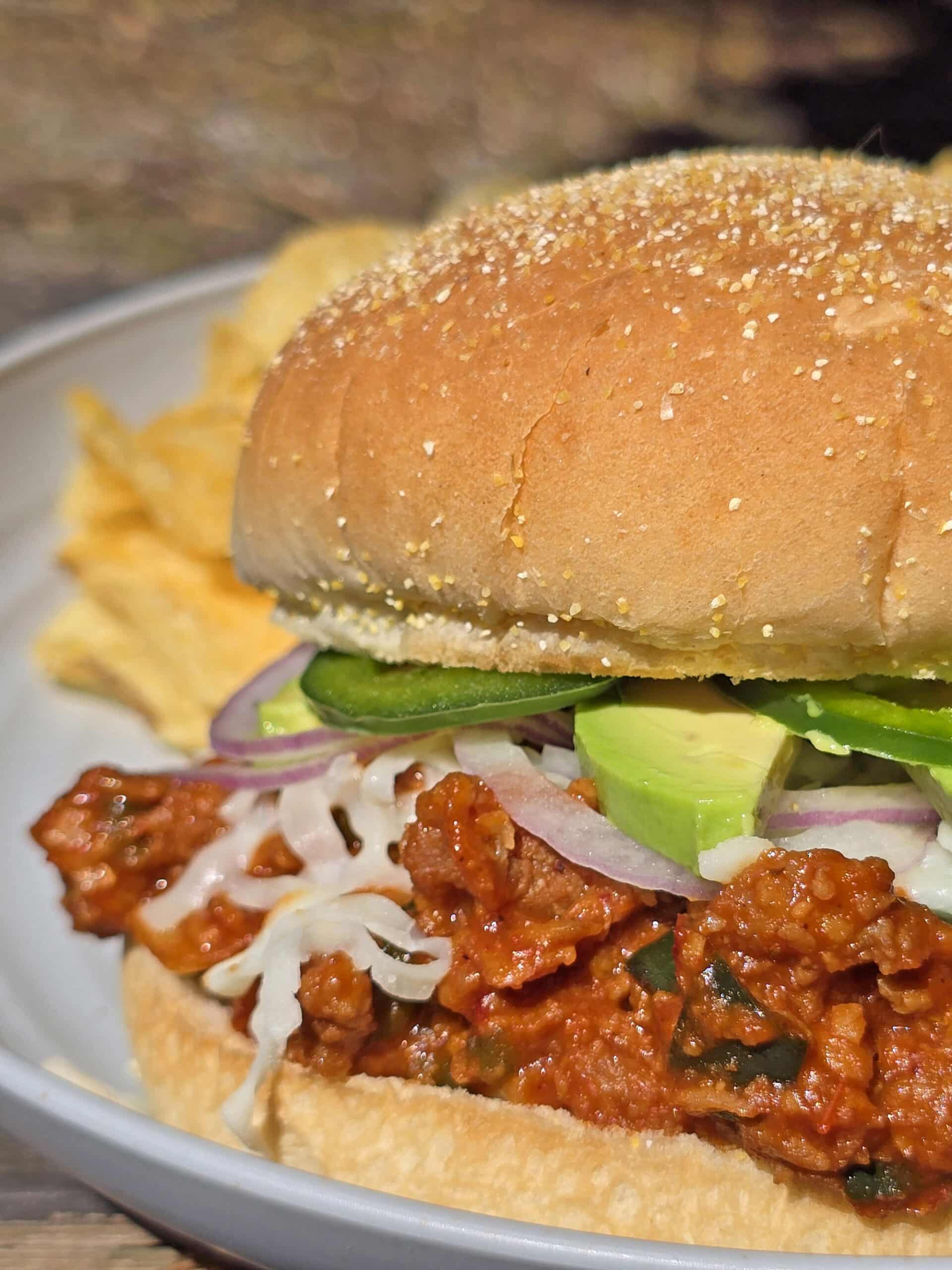 A Mexican sloppy Jose sandwich, with Monterey Jack, sliced jalapenos, and avocado, on a plate.